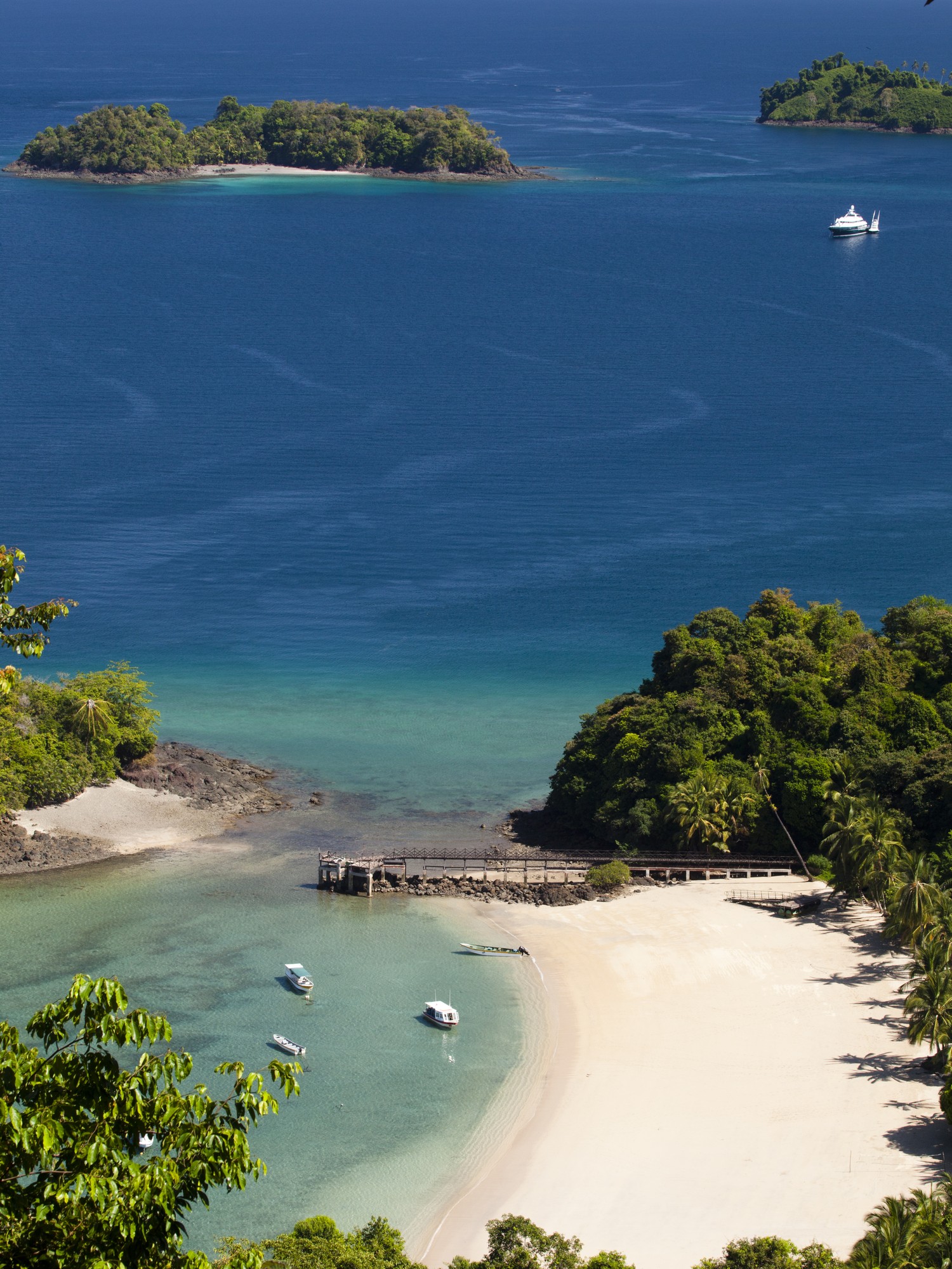 Aerial view of a secluded white-sand beach cove at Islas Secas with small boats anchored offshore and a yacht beyond the reef.
