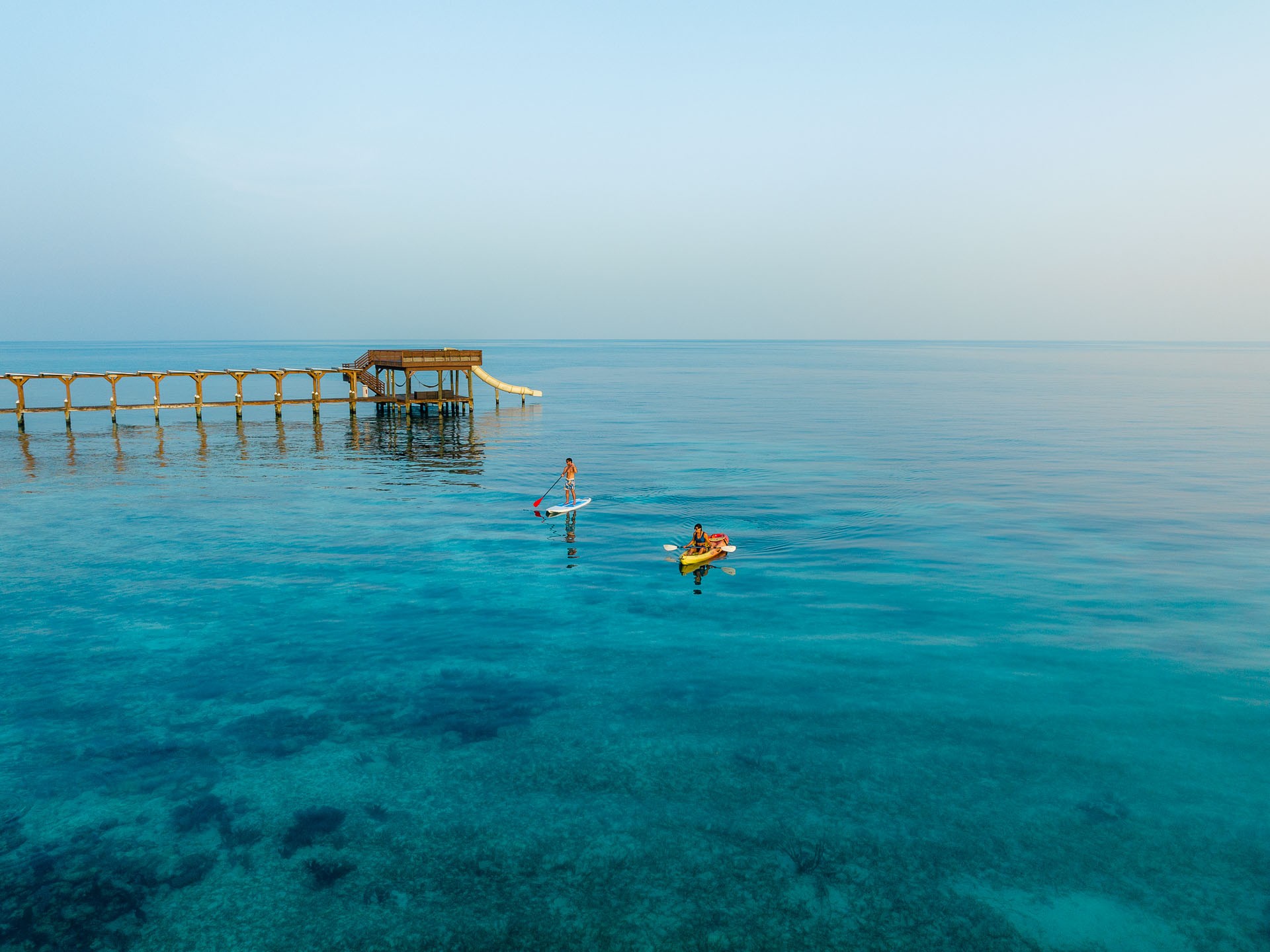 Paddleboarder and kayaker near an overwater dock at Ray Caye at sunrise.