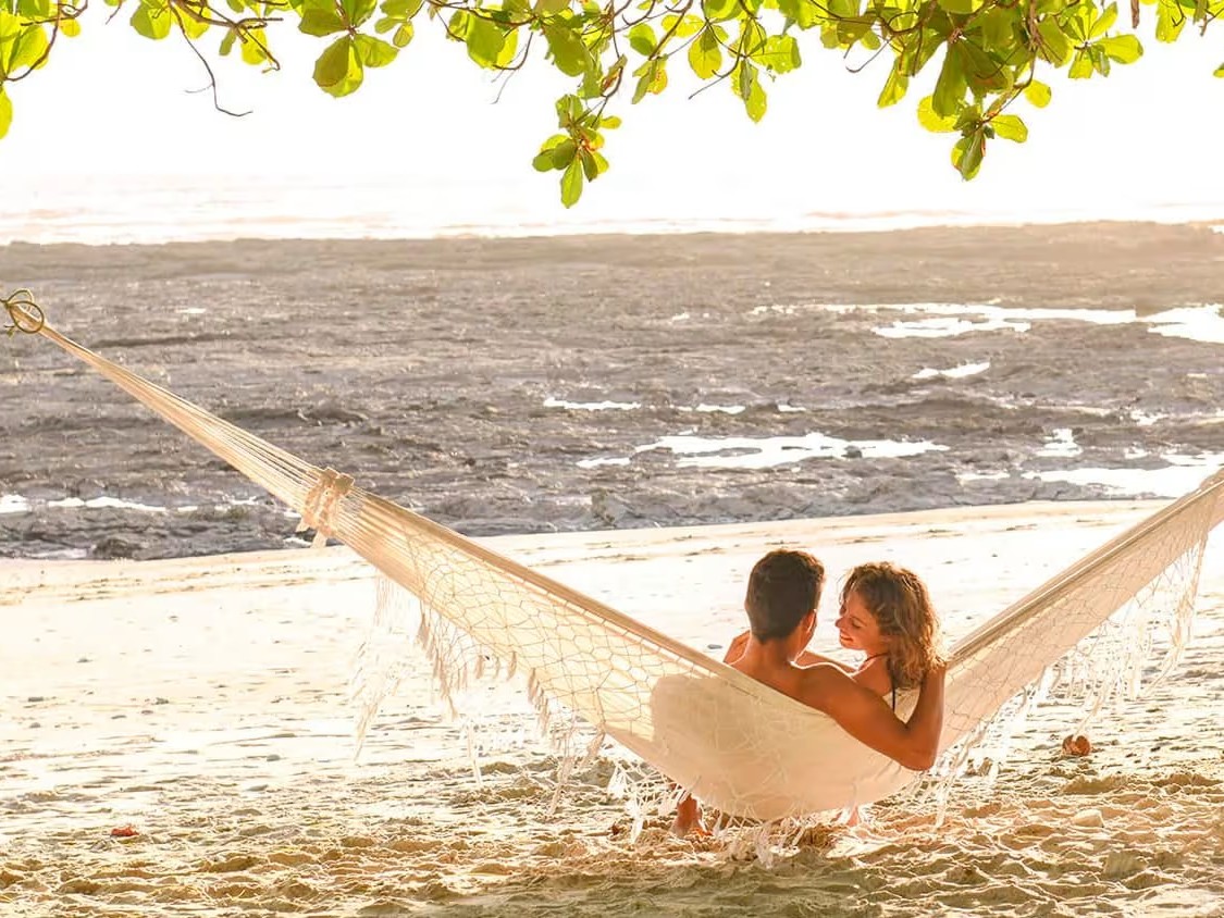 A couple relaxes together in a beachside hammock at Las Catalinas as the tide rolls in at golden hour.