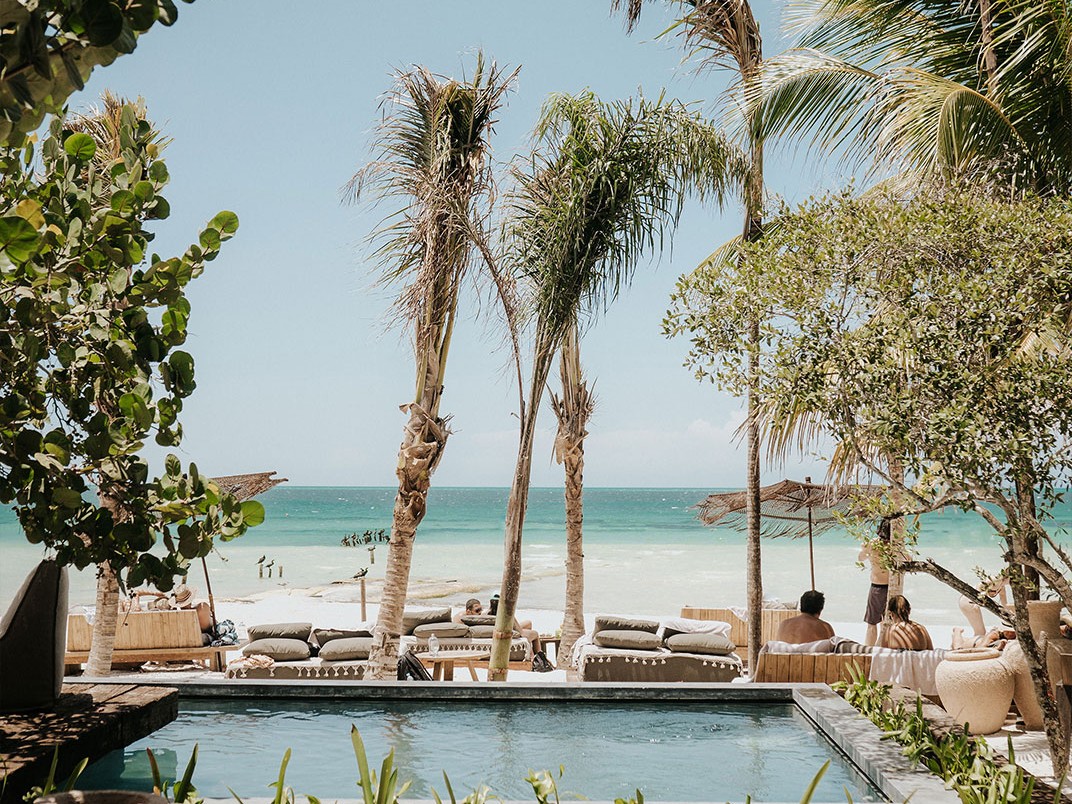 Shaded poolside lounge overlooking a sandy beach and the sea.