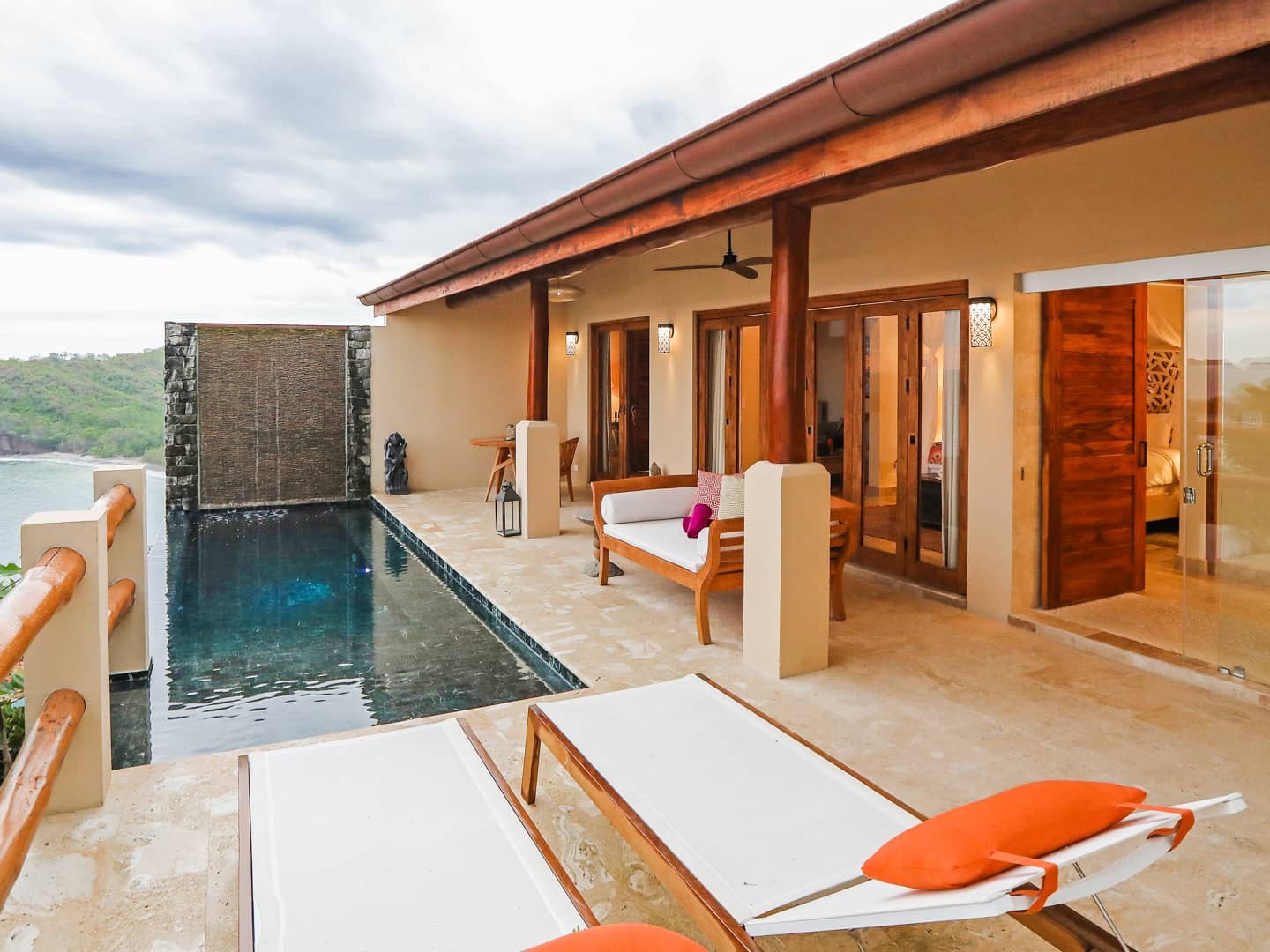 A hillside villa suite with a private plunge pool and glass doors opening to sweeping ocean views.