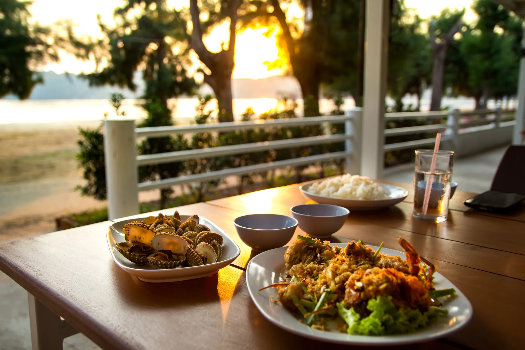 Seafood dishes and rice on a table at sunset with ocean and trees in the background. Oceanfront restaurant, Caribbean.