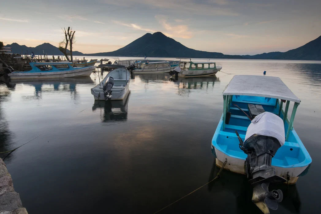 Small boats docked on calm lake water with volcanoes and mountains in the background at sunset. Lake Atitlan, Guatemala.