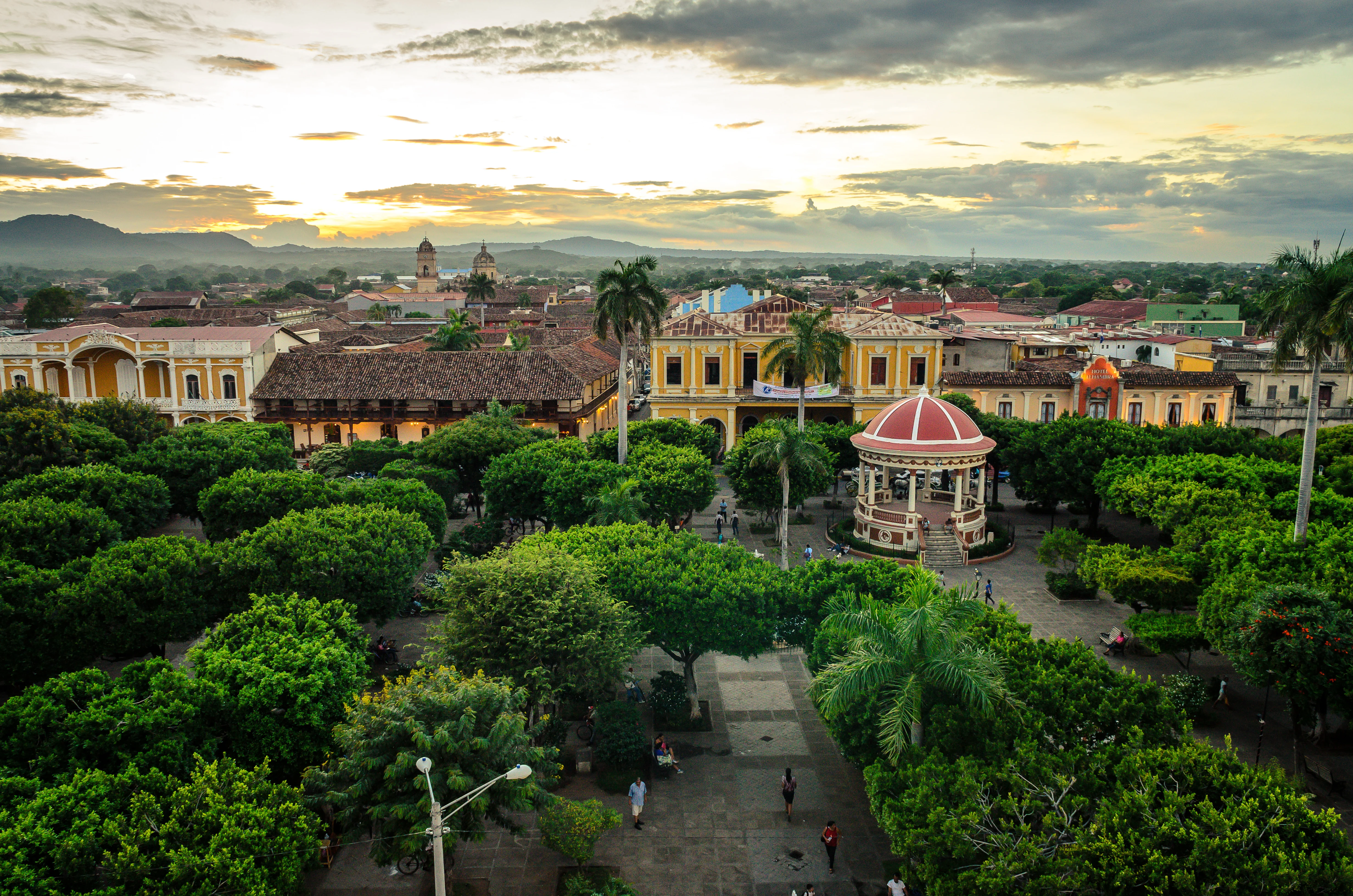 Central park with a pavilion surrounded by trees and colonial buildings under a cloudy sunset sky. Granada, Nicaragua.