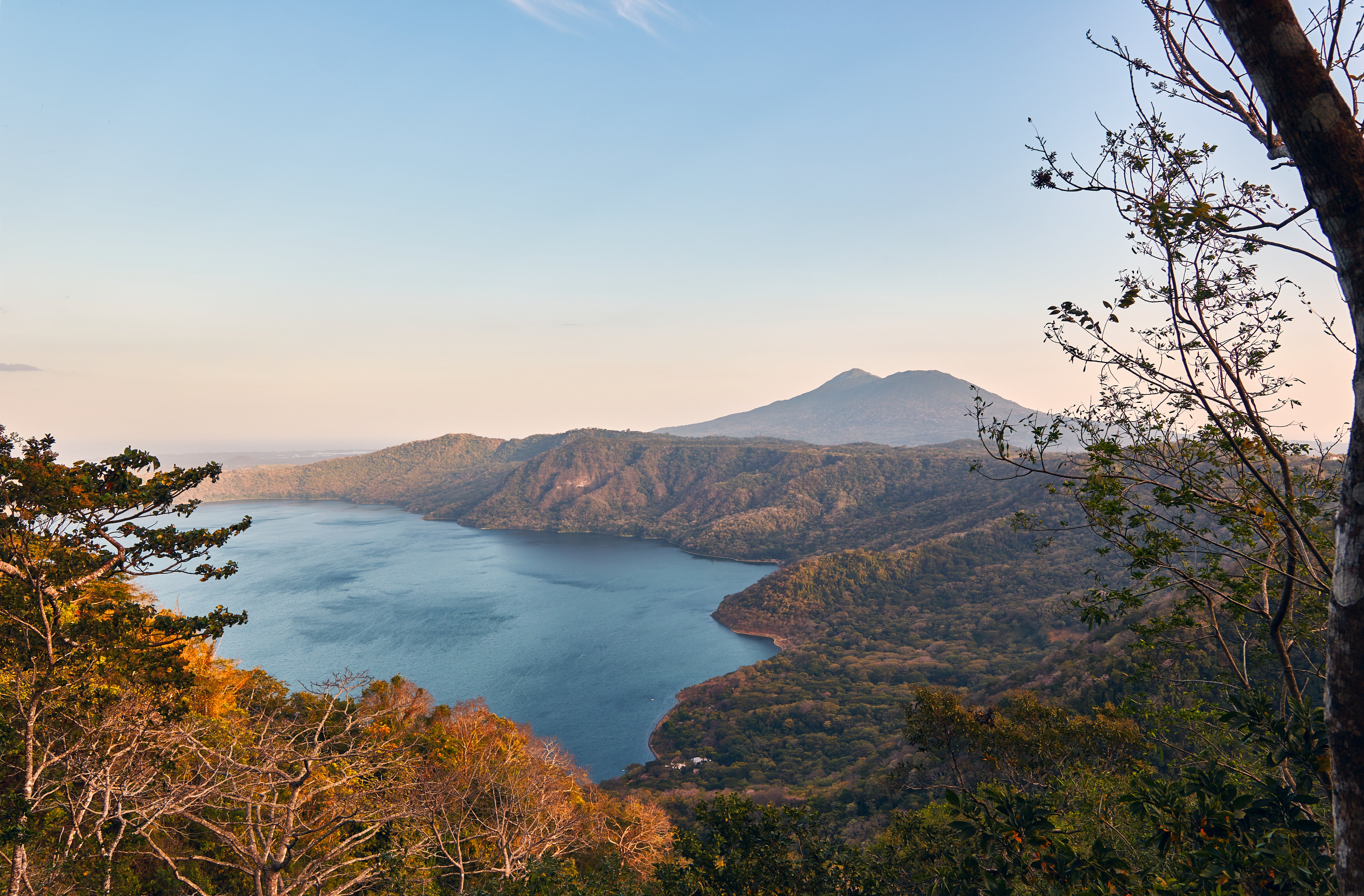 Scenic view of a blue lake surrounded by lush forest and mountains under a clear sky at sunset. Apoyo Lagoon, Nicaragua.