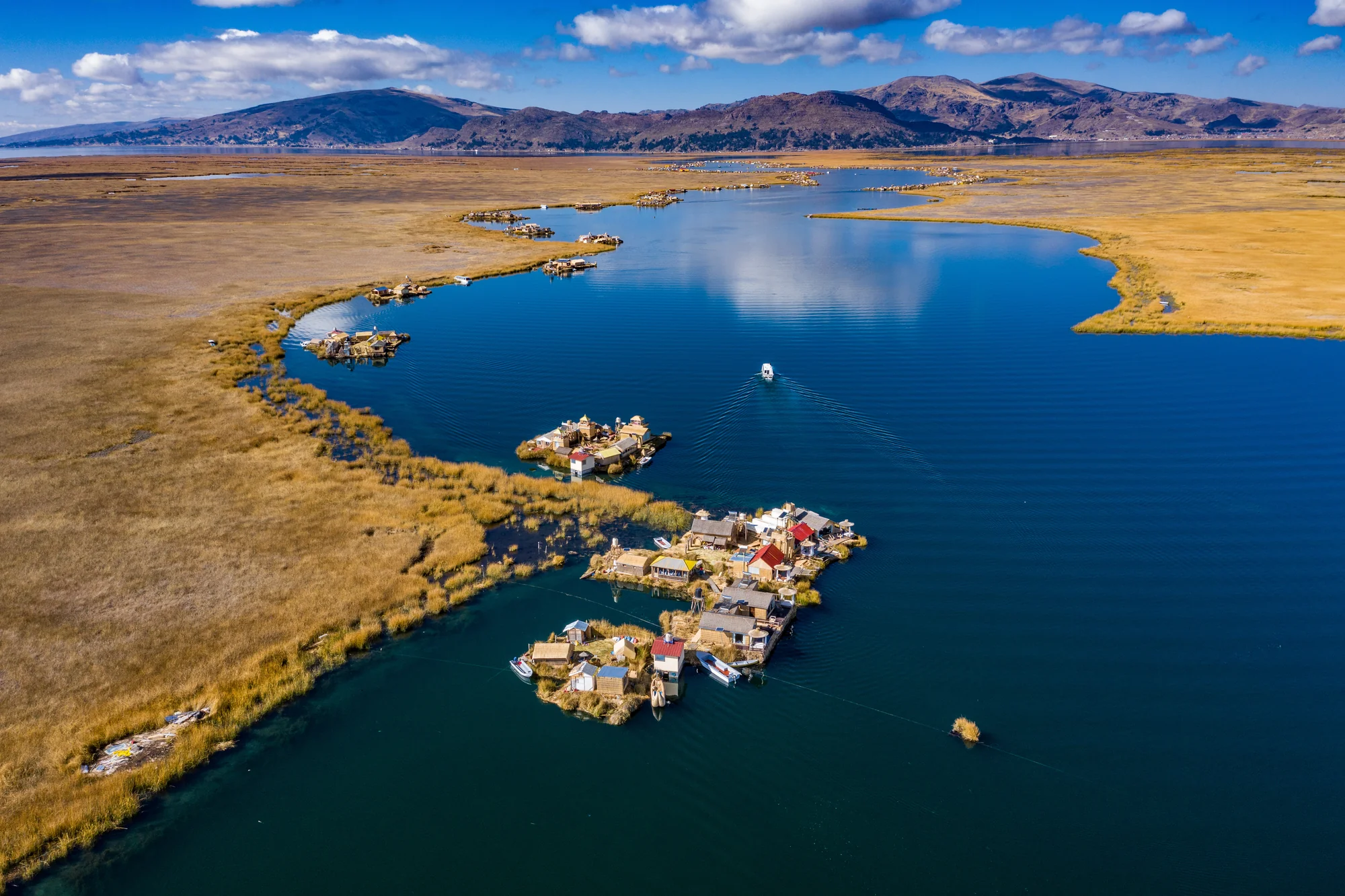 Aerial view of floating reed islands with houses on a lake surrounded by dry grass and mountains. Lake Titcaca, Peru.