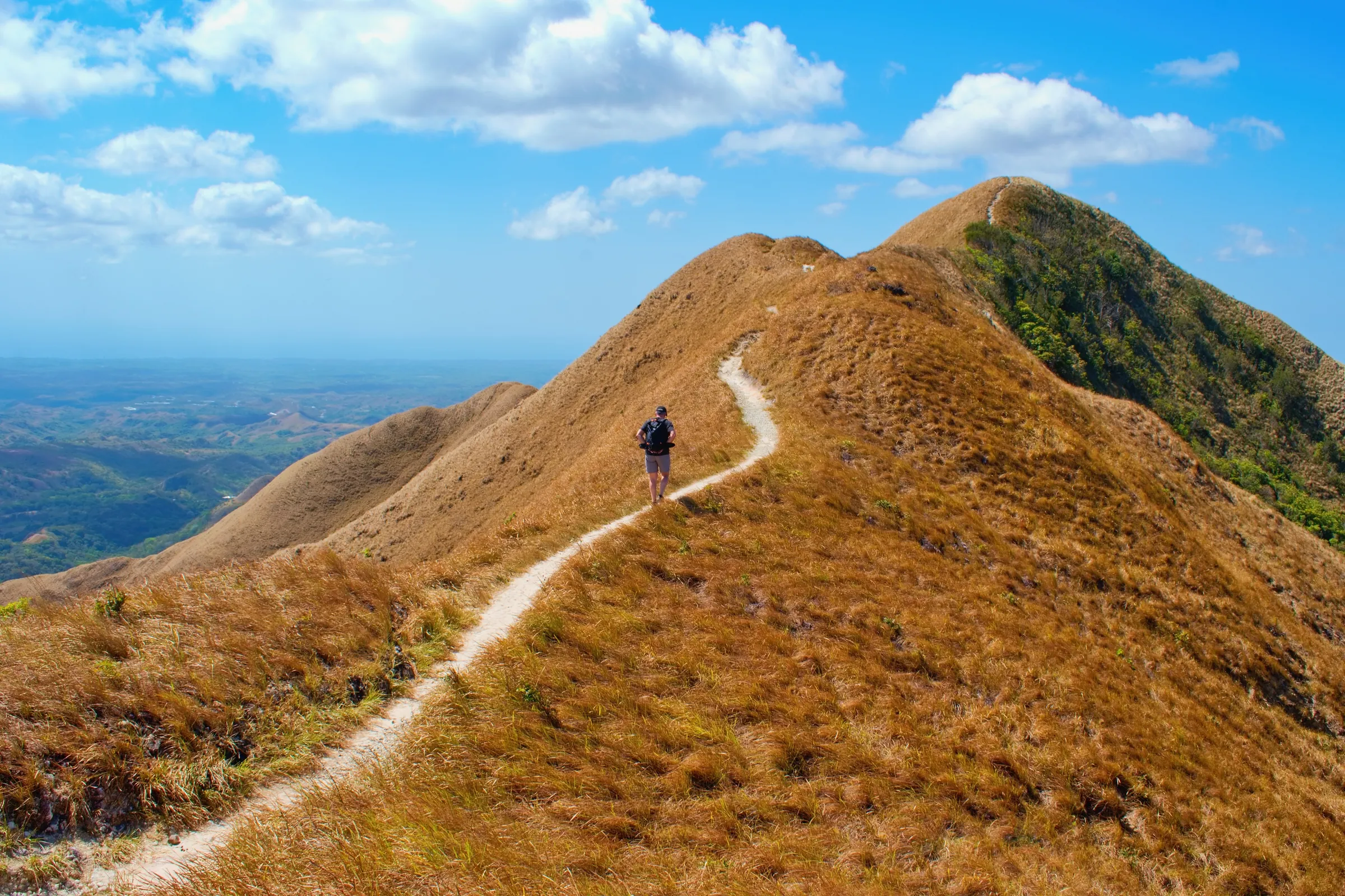 Hiker walking along a narrow grassy mountain ridge