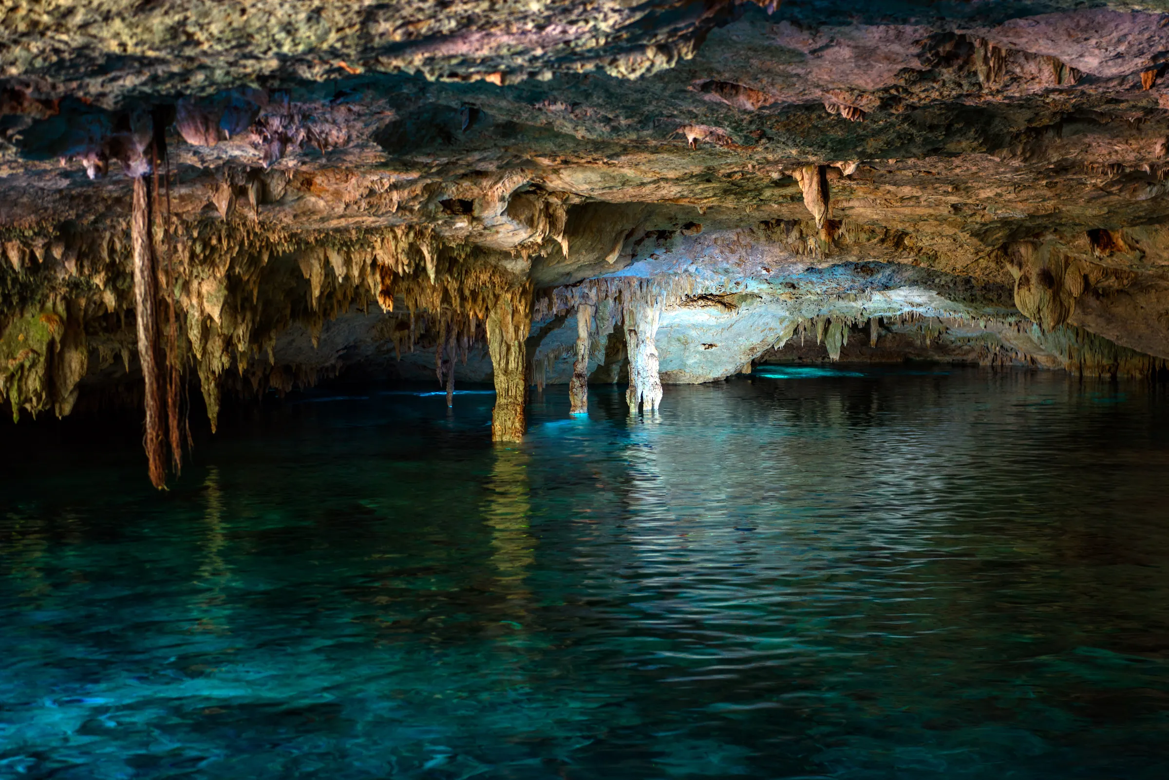 Clear water beneath stalactites in a cave cenote