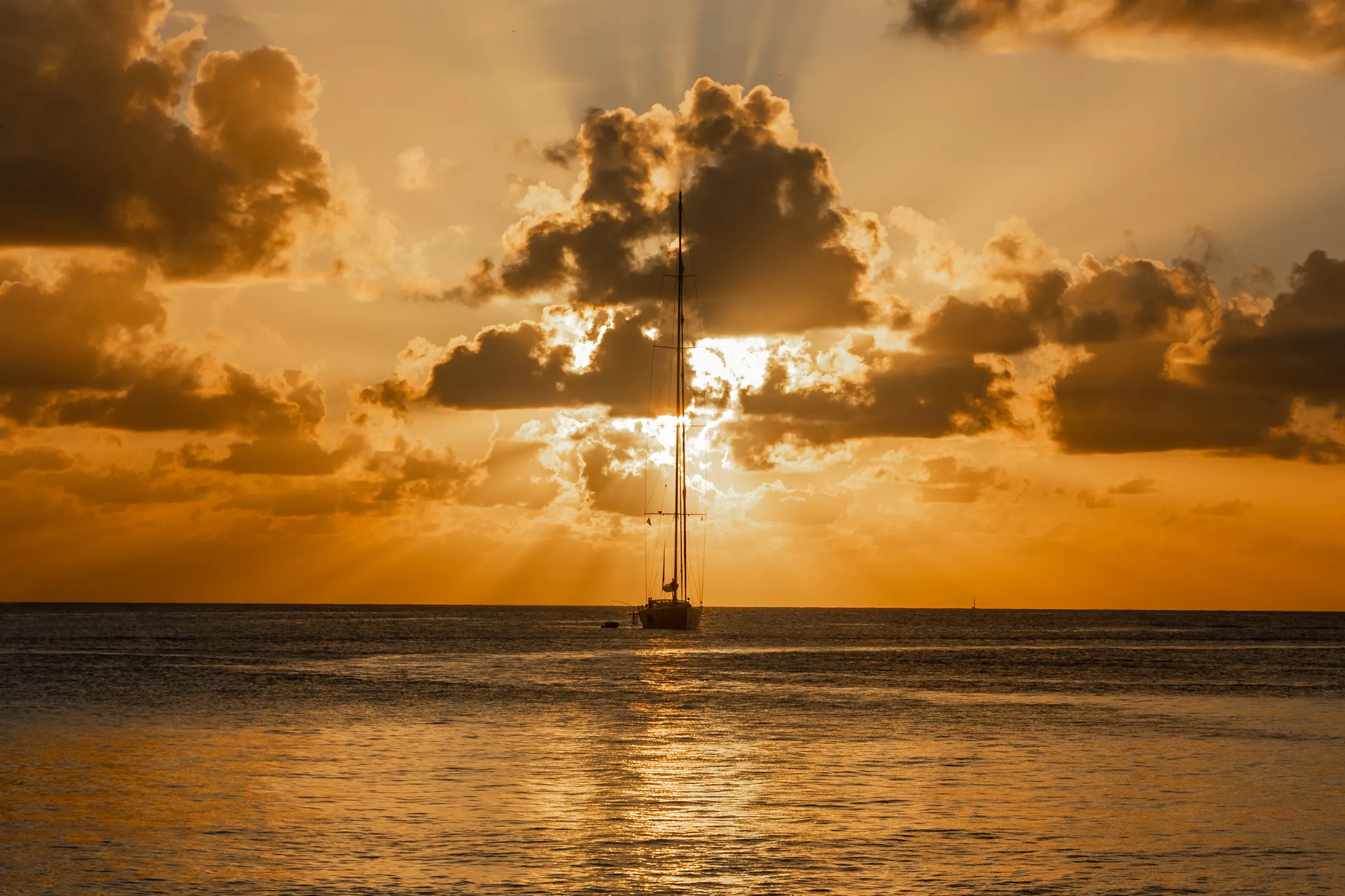 Sailboat silhouetted beneath golden sunset clouds