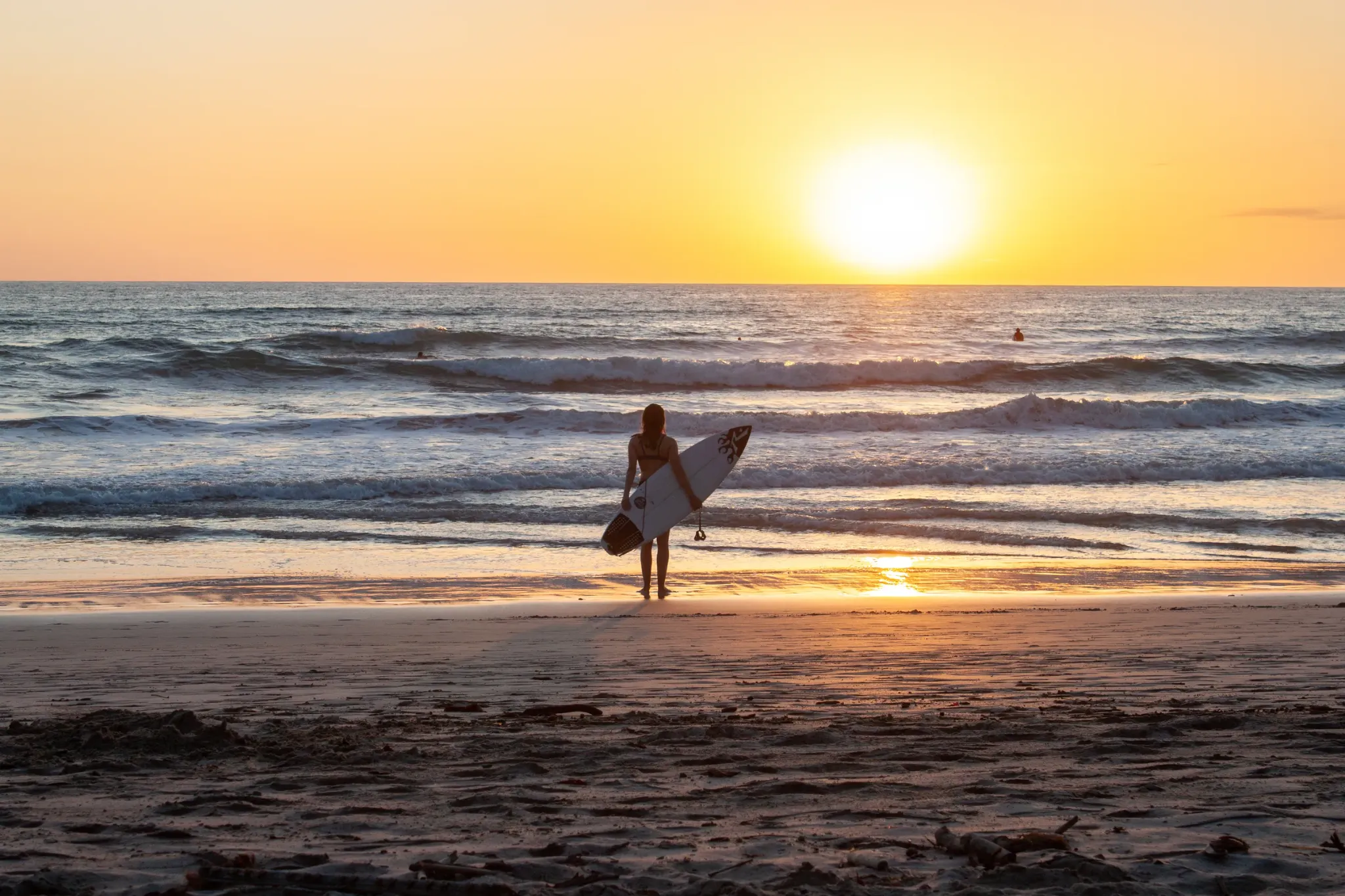 Surfer holding a board on the beach at sunset