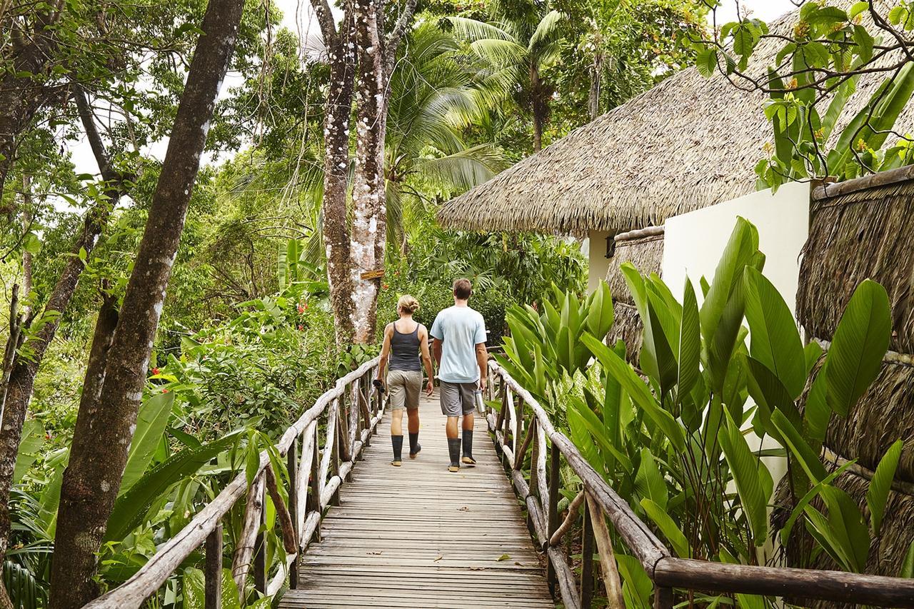 Two people walking on a wooden bridge in a tropical forest with a thatched-roof hut in the background; Lapa Rios, Osa Peninsula, Costa Rica