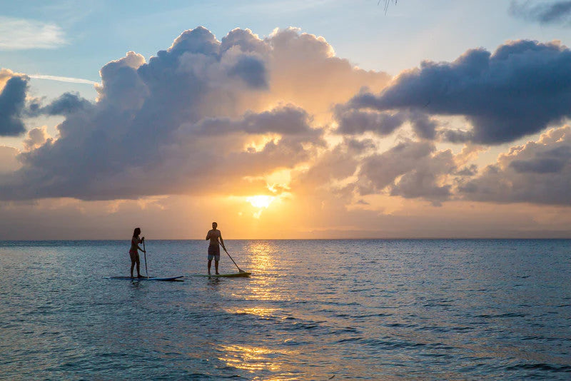 Couple paddleboarding together at sunset off Ray Caye, Belize