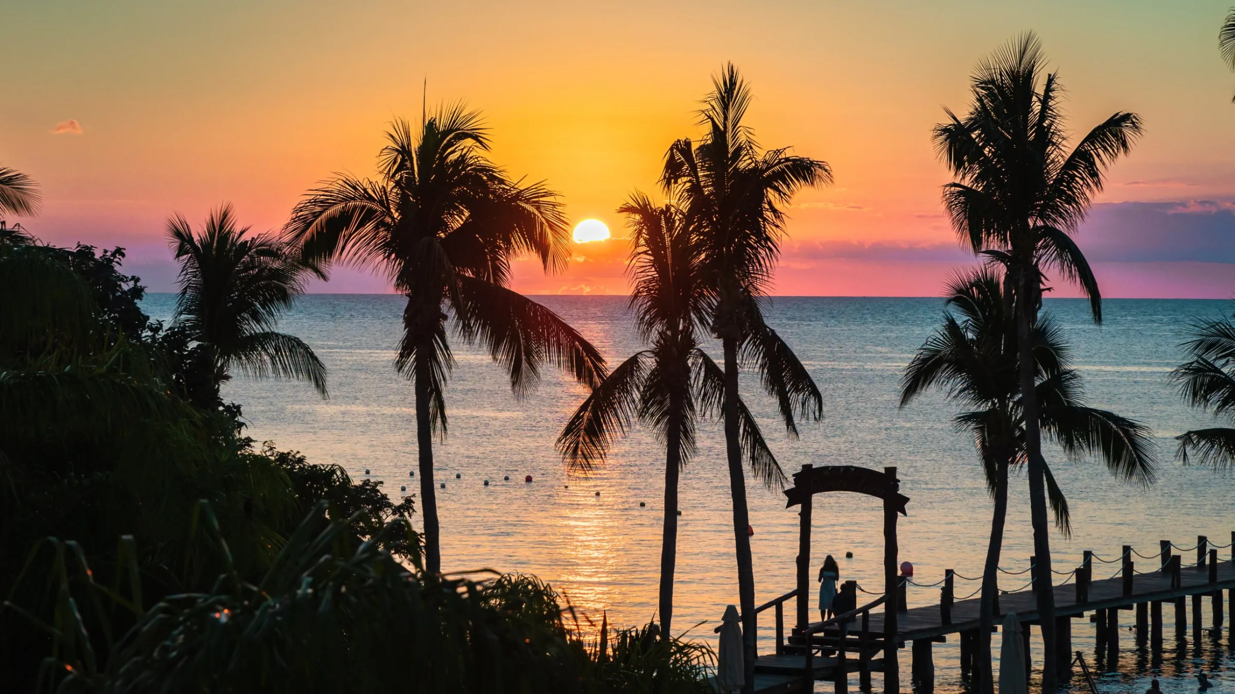 Sunset through palm trees over the sea and a wooden pier in Cozumel
