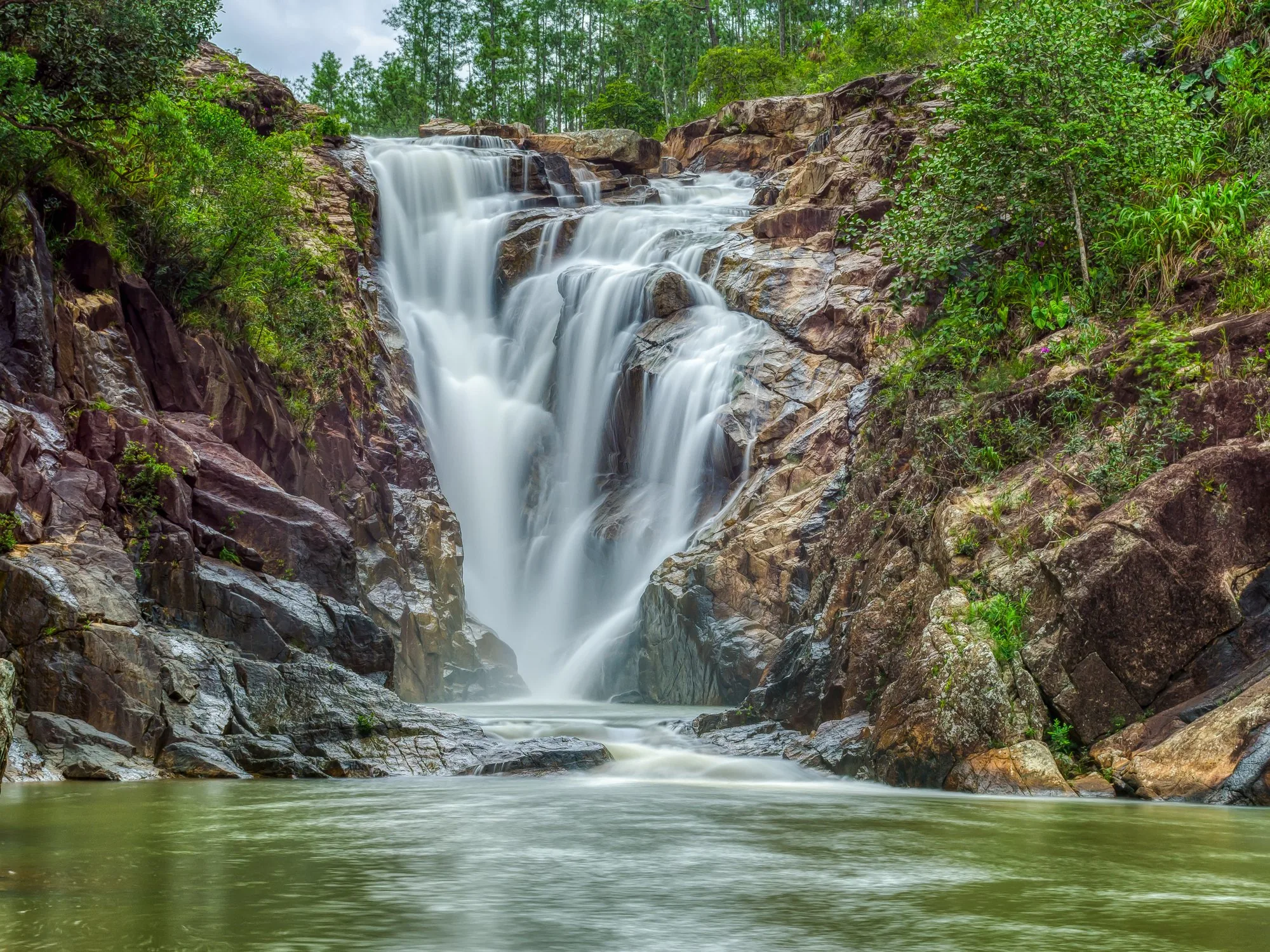 A wide jungle waterfall cascades over granite rock into a pool in Mountain Pine Ridge, Belize. Big Rock Falls.