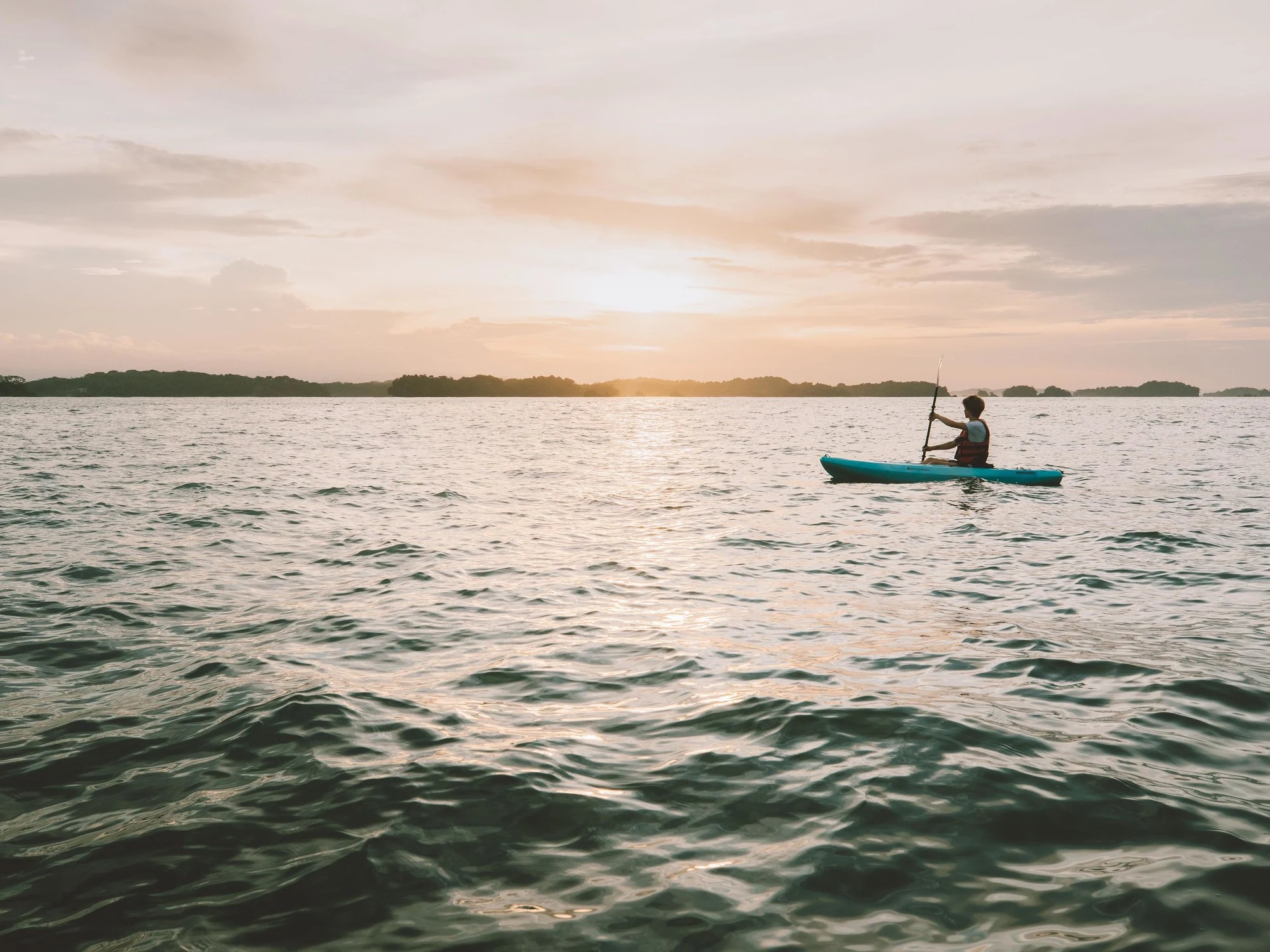 Silhouette of a kayaker paddling across calm water at sunset near Panama's Pacific coast.