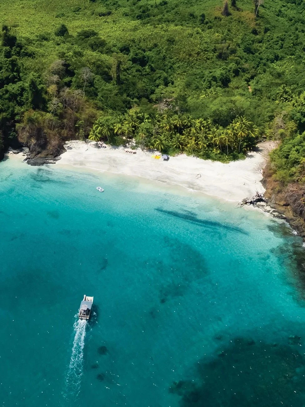 Aerial view of a boat approaching a secluded white-sand beach at Islas Secas, framed by dense jungle.