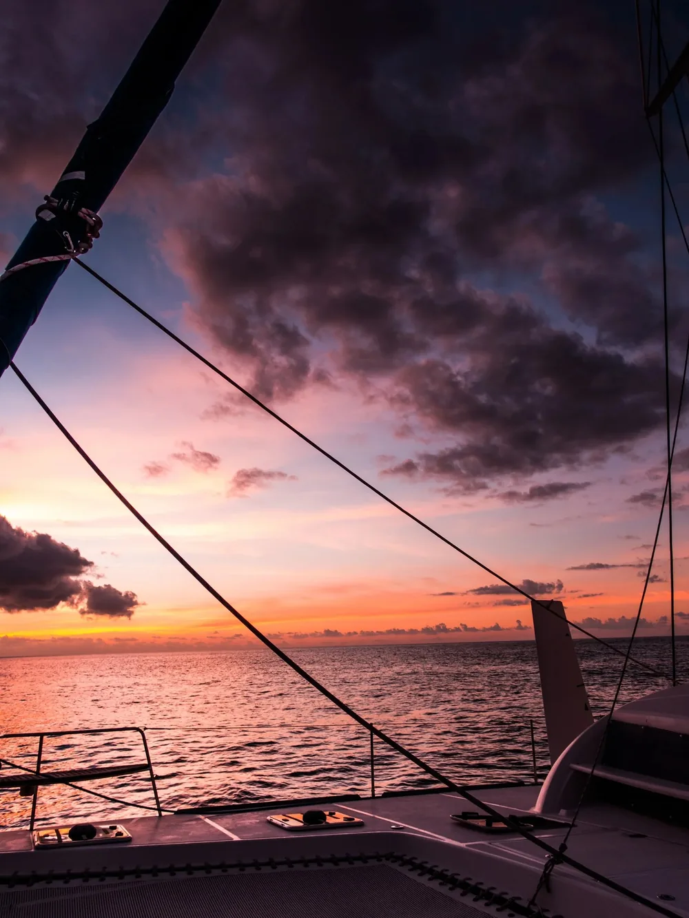 Sunset view from the deck of a catamaran, with rigging silhouetted against a pink and orange sky over the sea, Guna Yala, Panama.