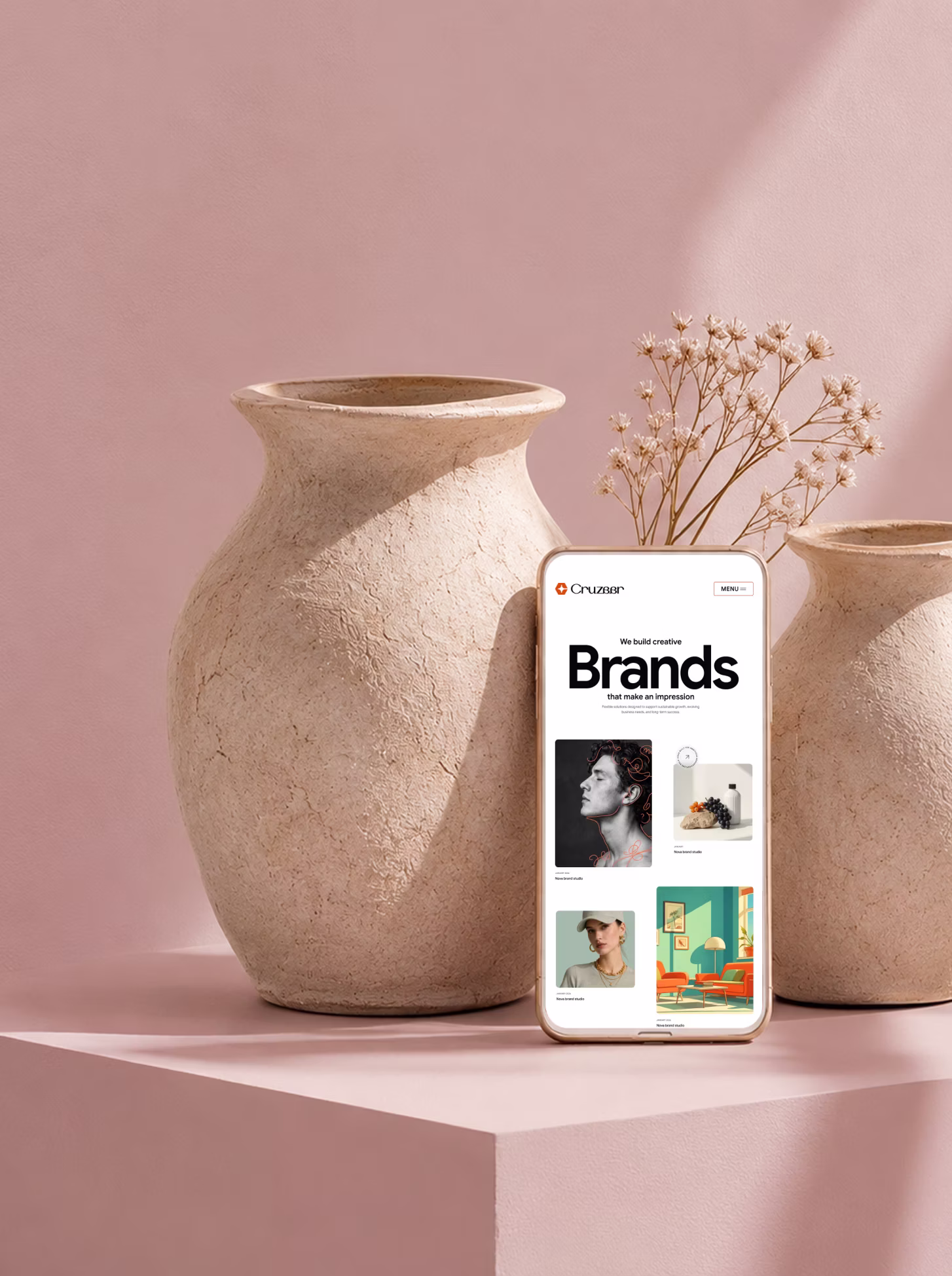 Smartphone displaying a creative branding website screen on a pink surface between two ceramic vases.