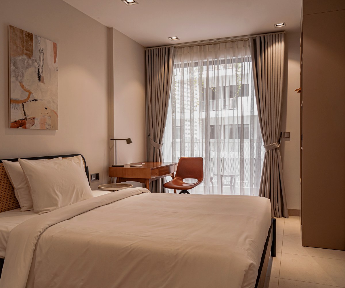 A furnished Commune Live room with bed, desk and balcony door