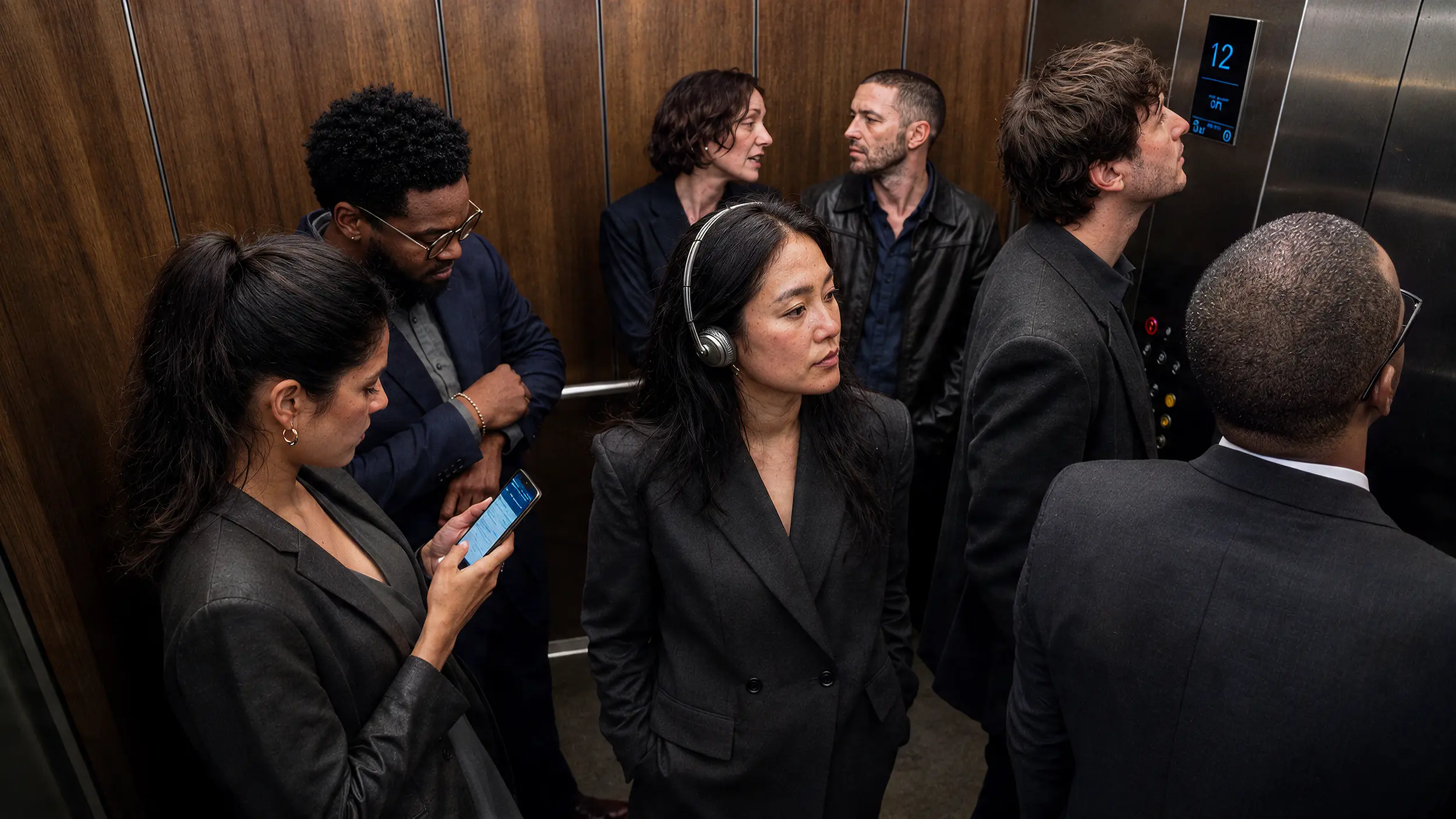 Group of professionals in dark business attire riding a wood-panelled elevator