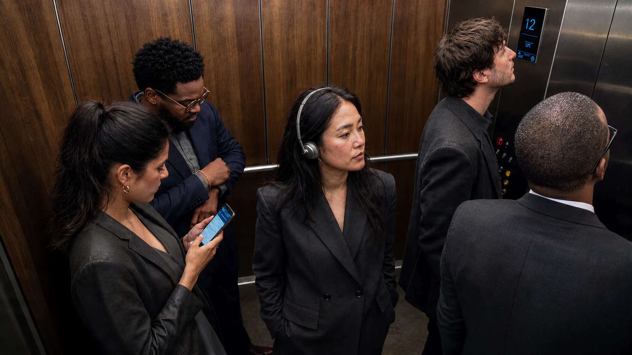 Group of professionals in dark business attire riding a wood-panelled elevator