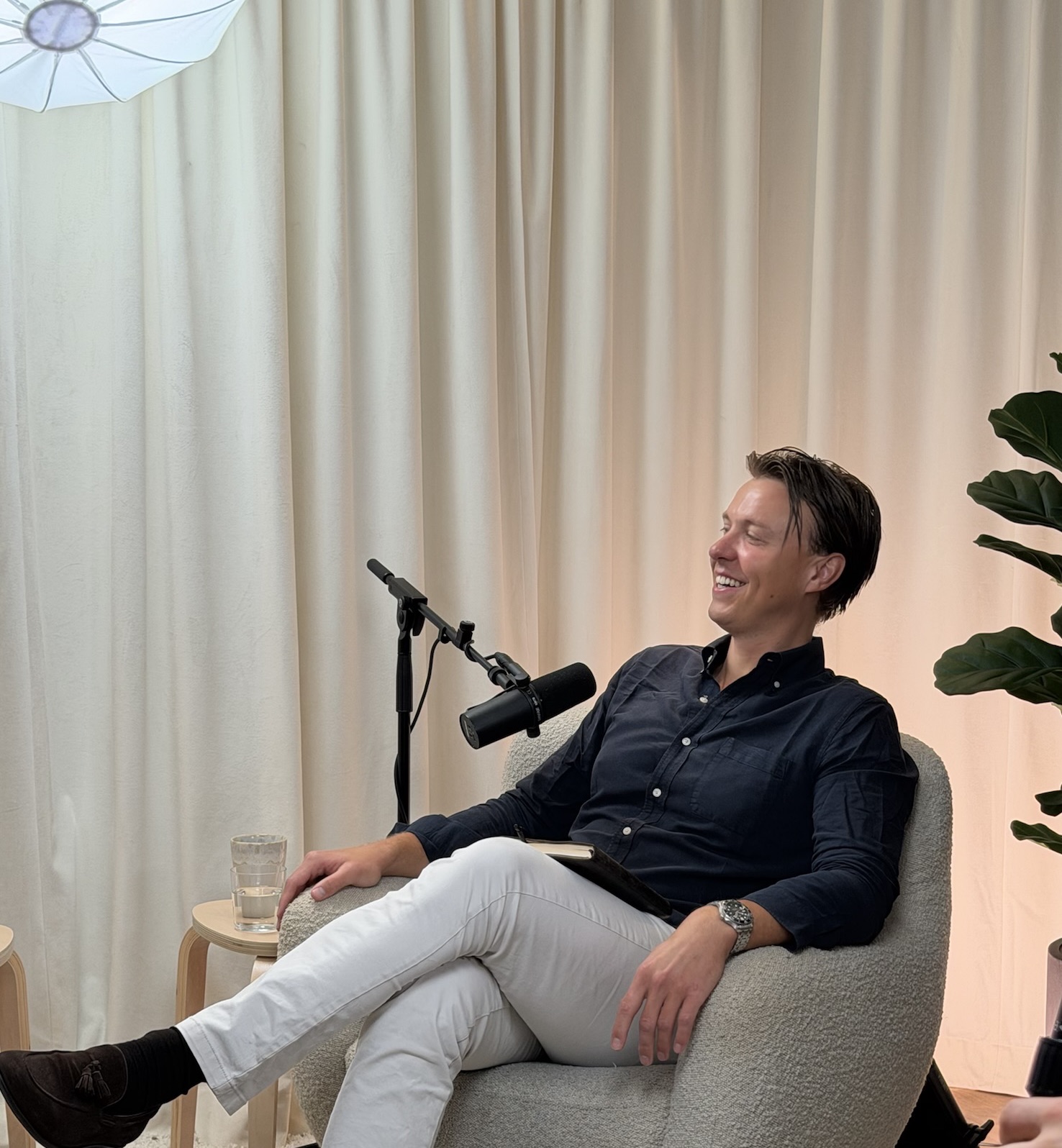 Martin M Eriksson i studion, tillbakalutad i fåtöljen framför en ljus gardinvägg