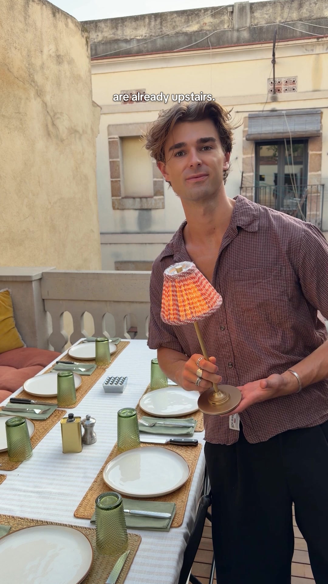 Shawn Fortune holding Corston’s red pleated rechargeable lamp beside a table set for dinner.