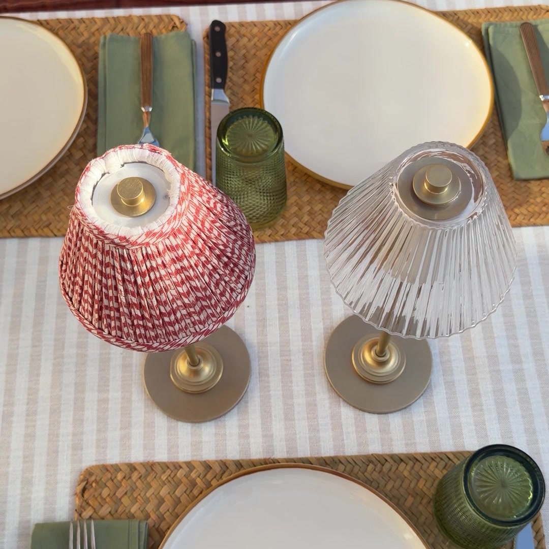 Lámparas recargables Corston, una con pantalla plisada roja y otra con pantalla de vidrio acanalado, en una mesa preparada para cenar.