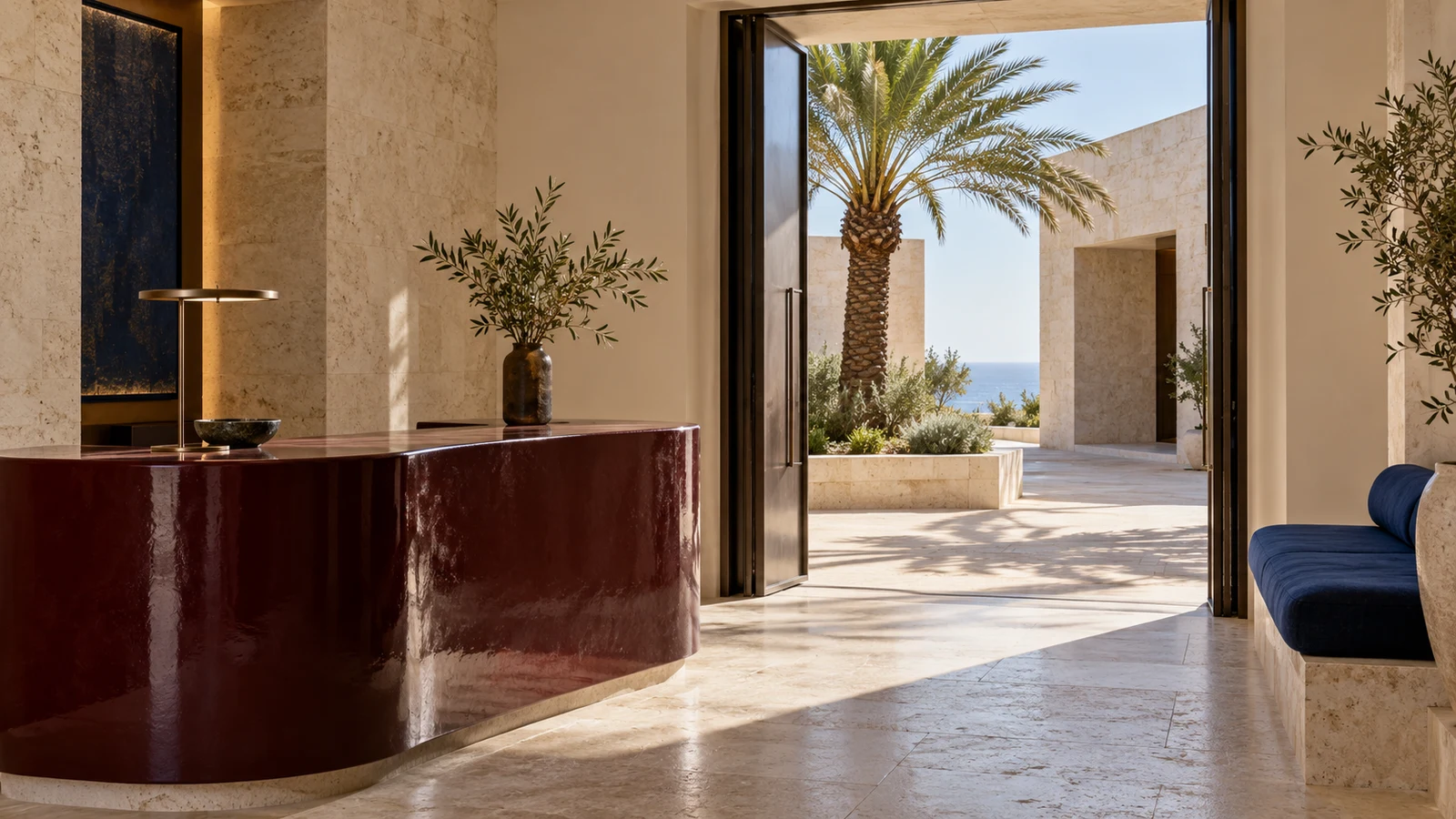 Oxblood reception desk and blue seating opening onto a sunlit hotel courtyard.