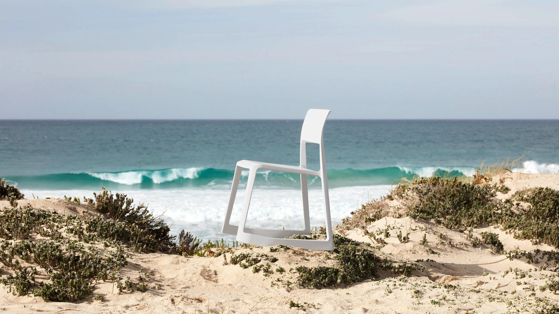 A white Vitra Tip Ton chair photographed in profile on a sandy coastal landscape.