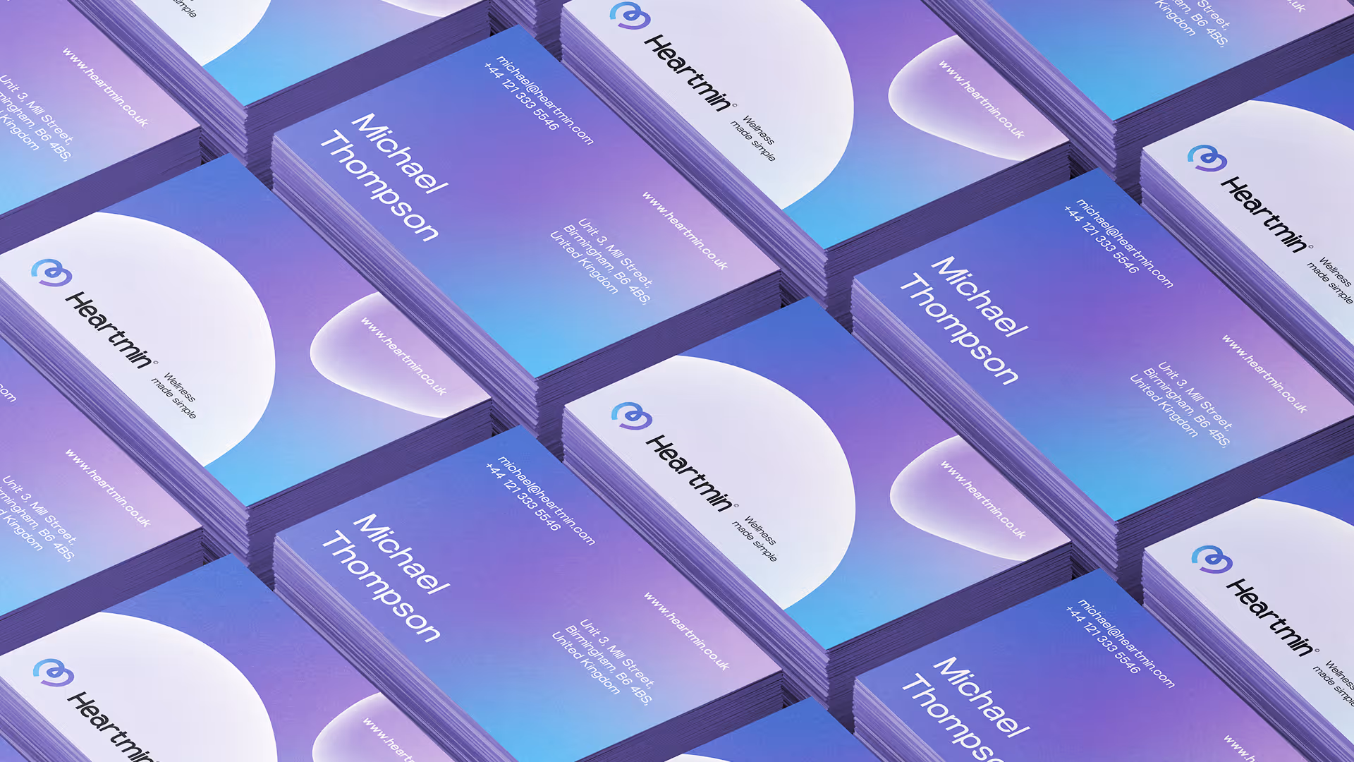 Stacks of purple and blue gradient business cards for Michael Thompson with Heartmin logo and contact details.