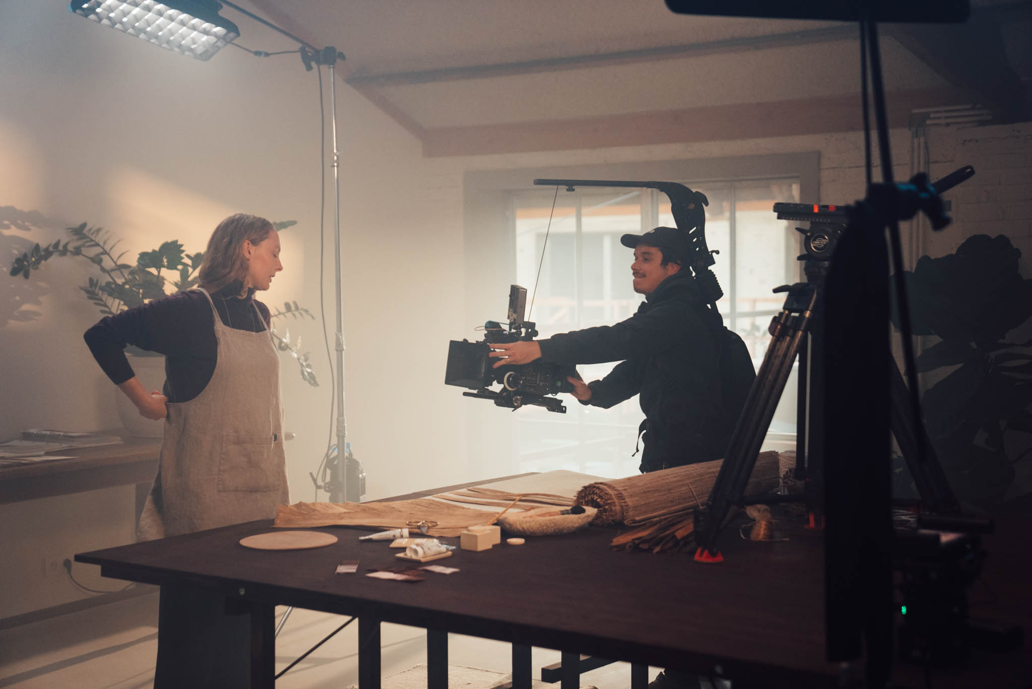 Camera crew filming a craftsman at a workbench in soft light