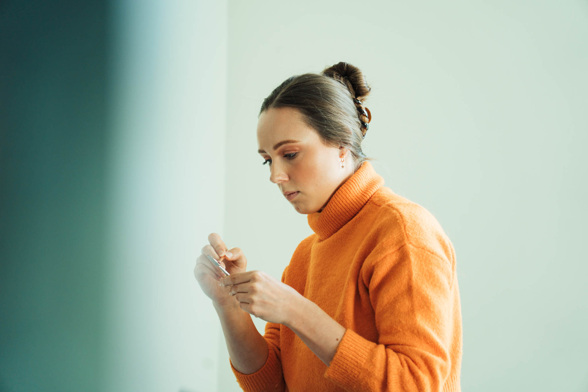 Woman in an orange sweater concentrating on a small object