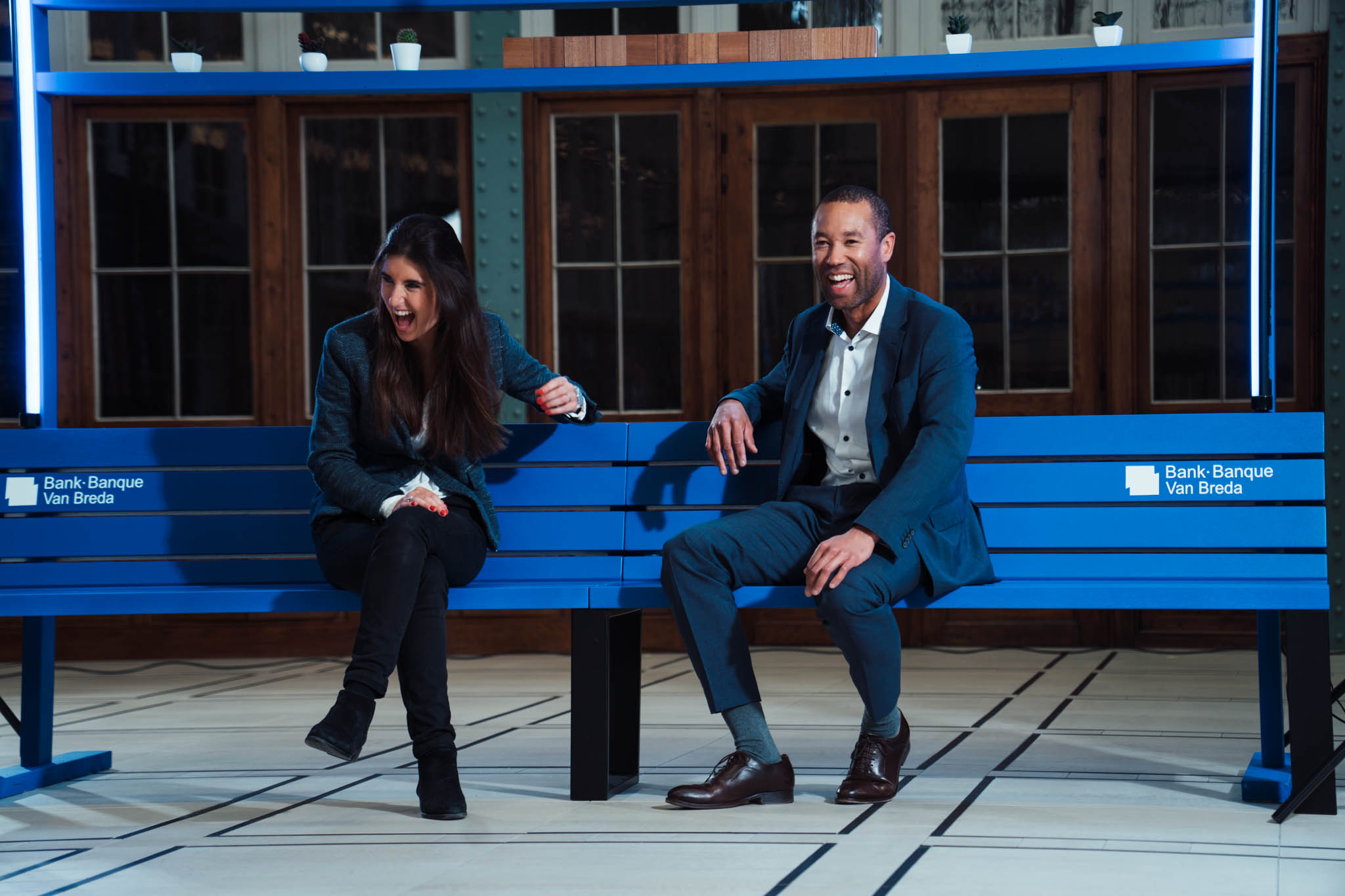 Two people laughing on a blue bench on a studio set