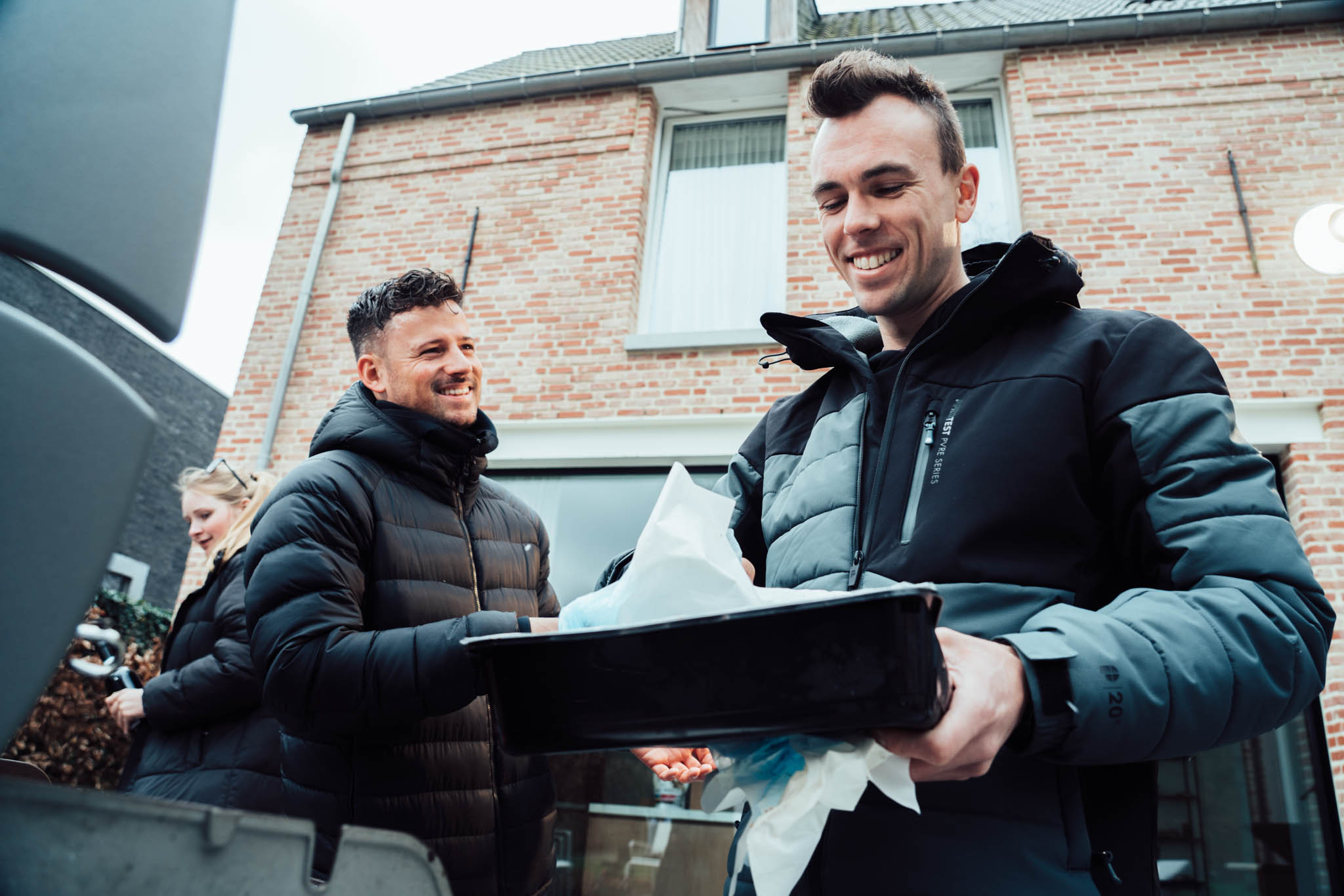 Two men smiling while unpacking equipment outside a house