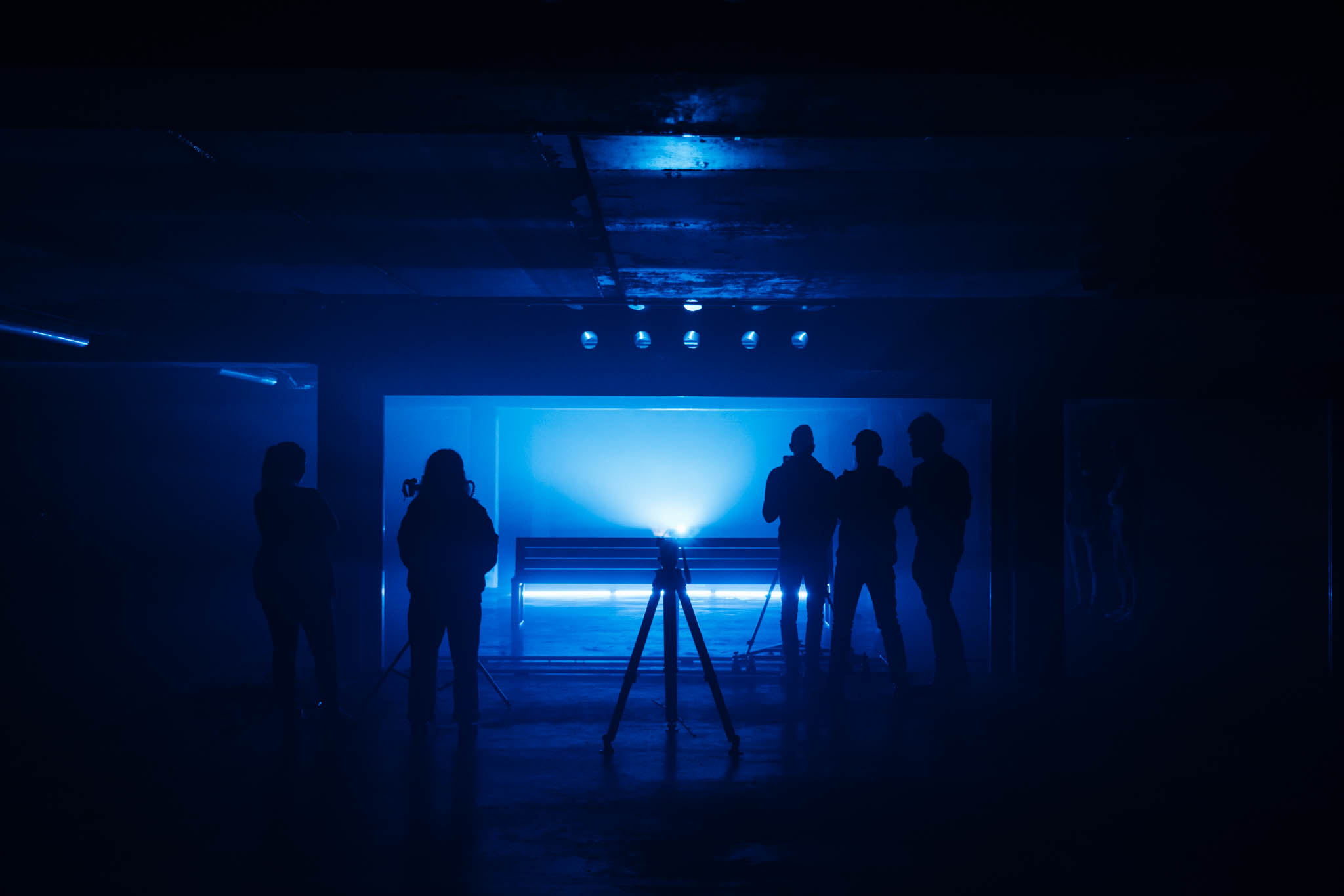 Silhouettes of a film crew in a dark room lit by blue light