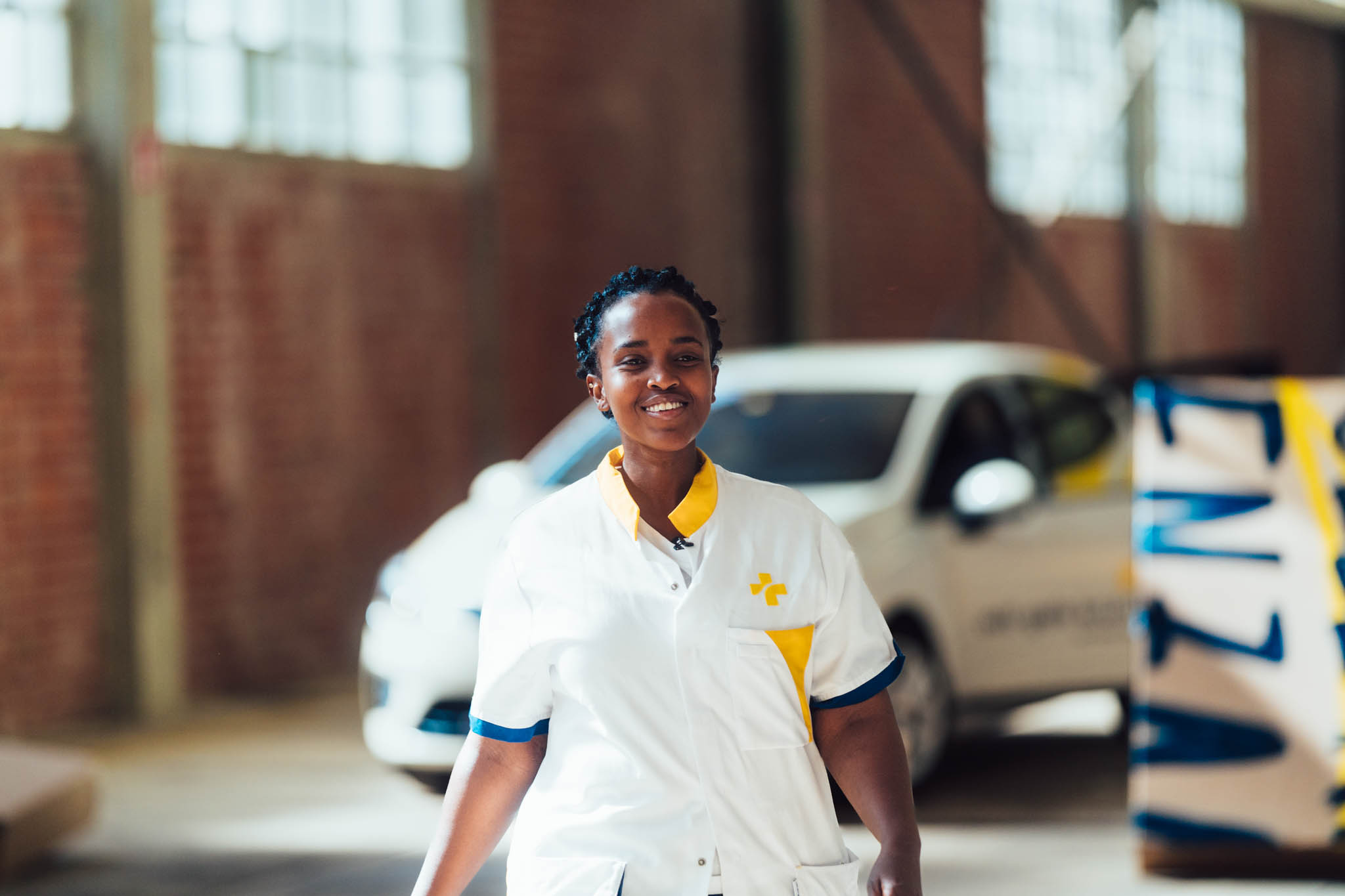 Smiling Wit-Gele Kruis nurse in uniform next to a company car