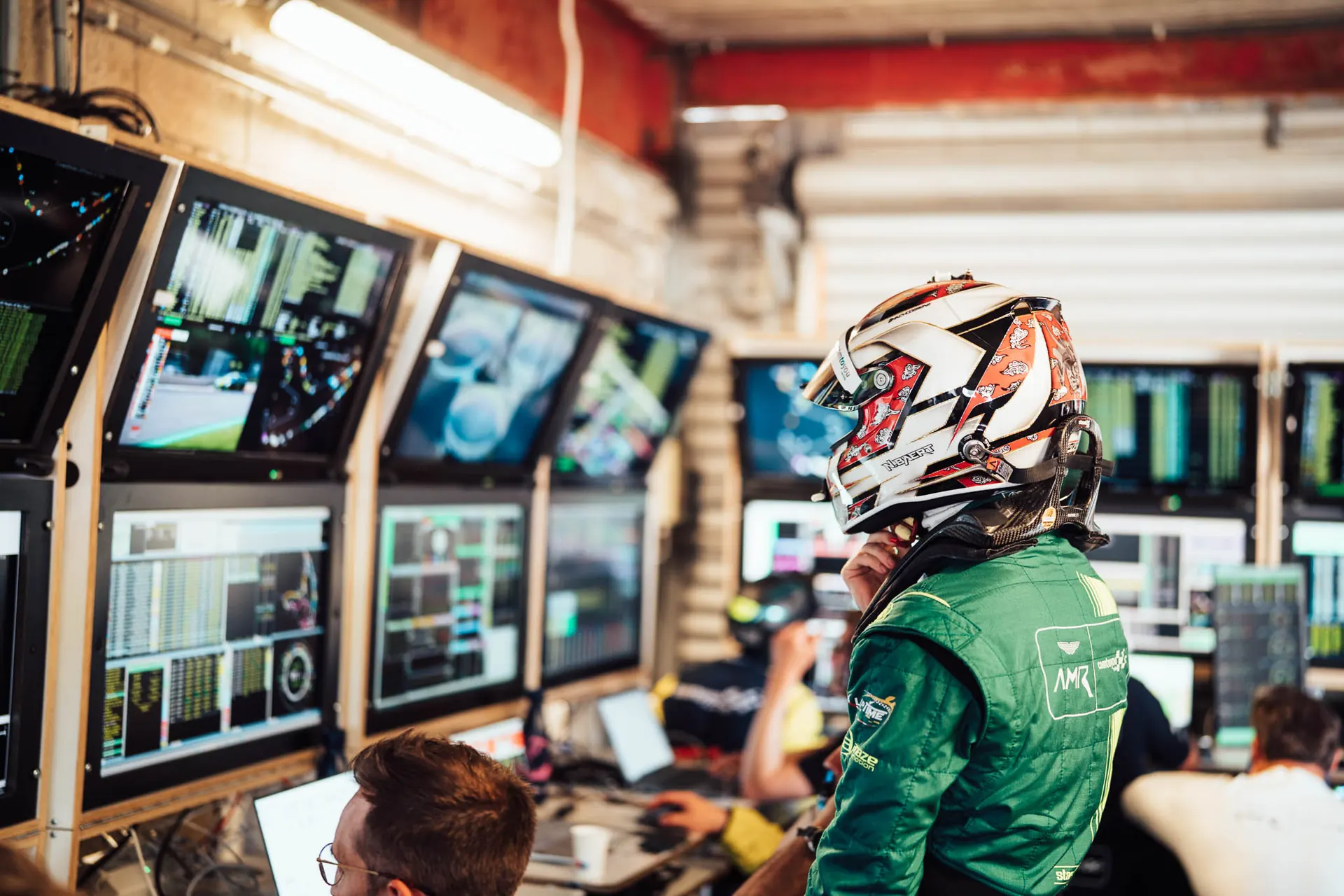 Racing driver in helmet watching timing screens in the team garage