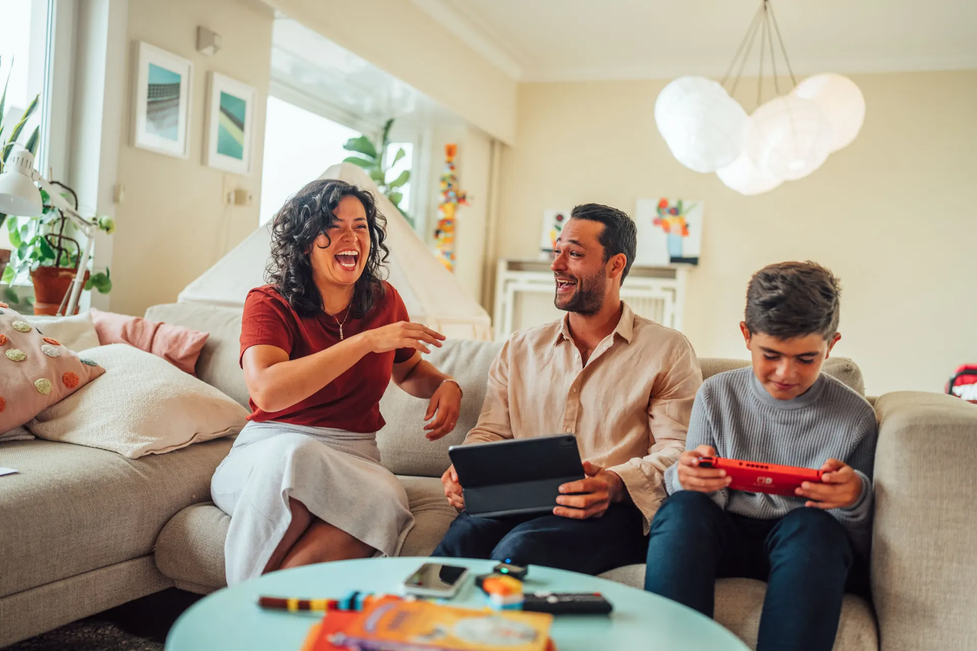 Family laughing on the sofa with a tablet and game console in the Eneco campaign