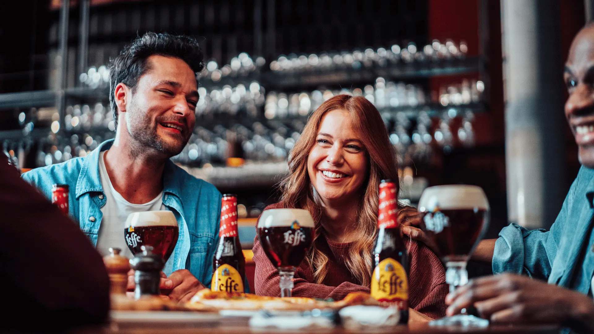 Friends laughing at a bar table with glasses of Leffe