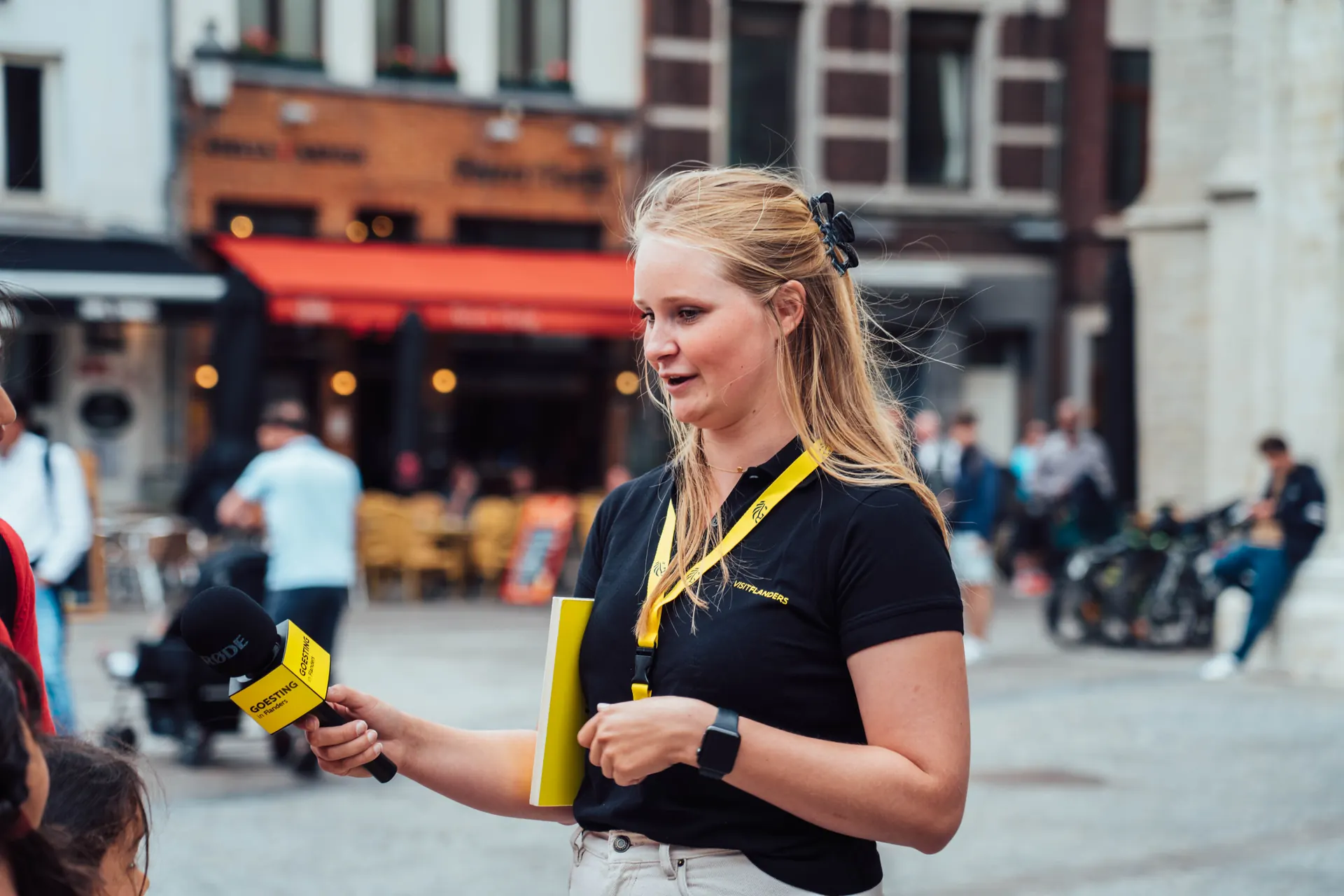 Presenter with a microphone interviewing people on a city square for Toerisme Vlaanderen