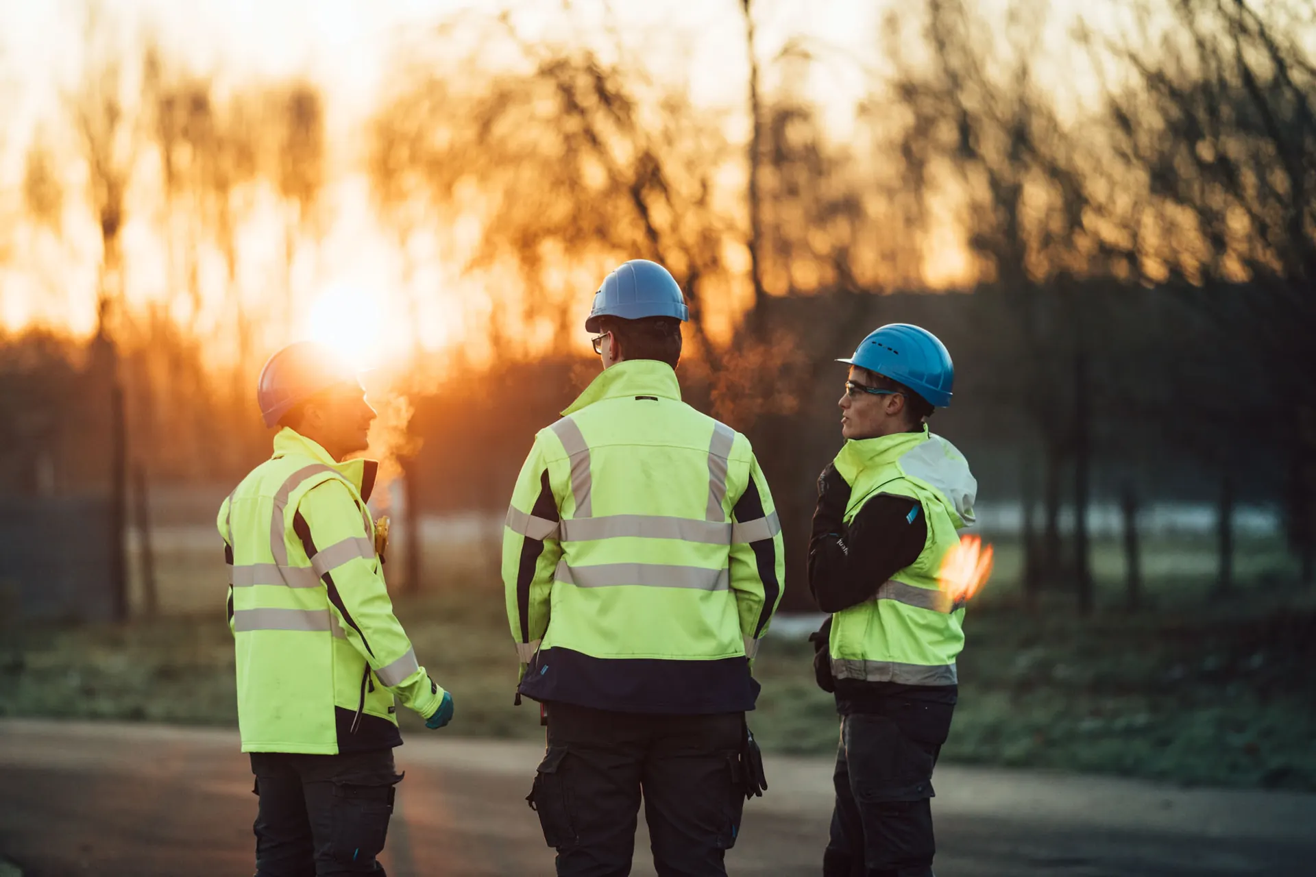 Three workers in hard hats and high-visibility jackets at sunset