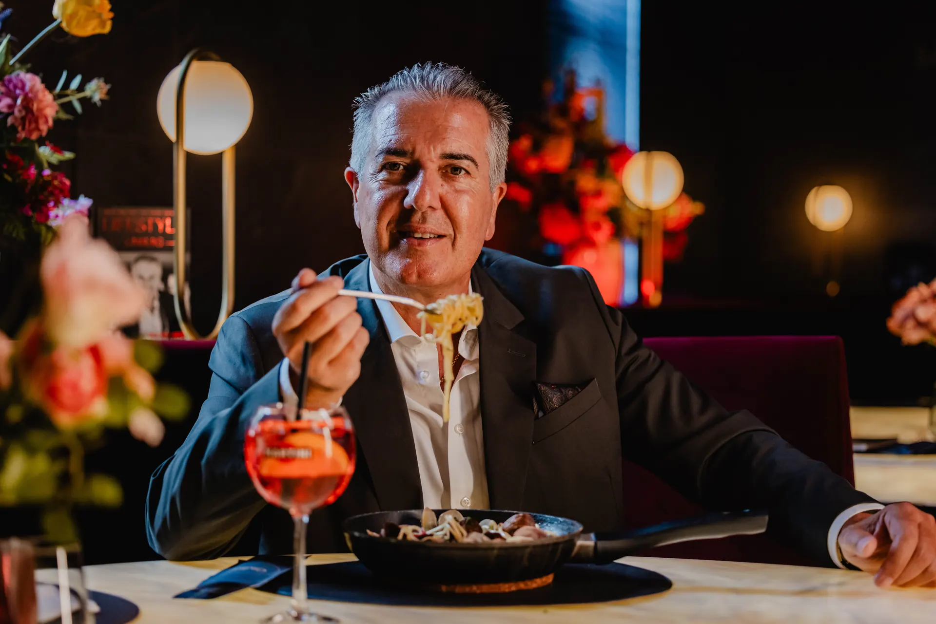 Man eating pasta at a restaurant table with a spritz cocktail