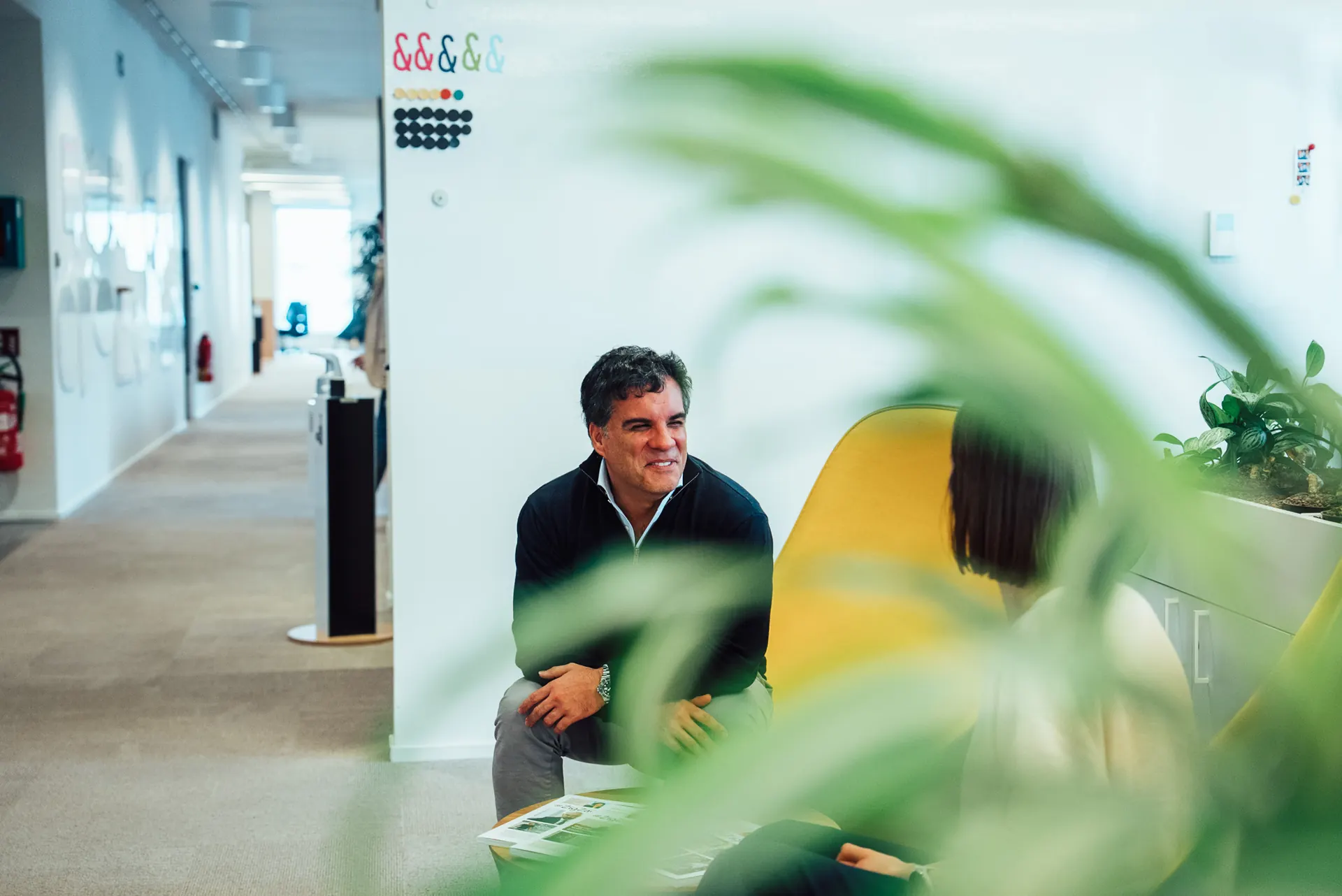 Man smiling during an interview in an office, framed through plants