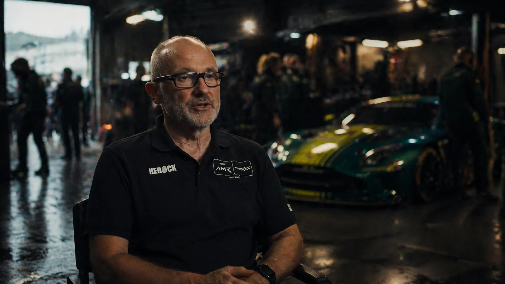 Team manager interviewed in a race garage with a GT car behind him