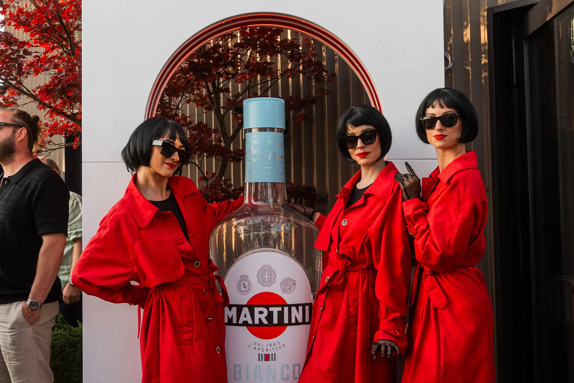 Three performers in red coats beside a giant Martini Bianco bottle