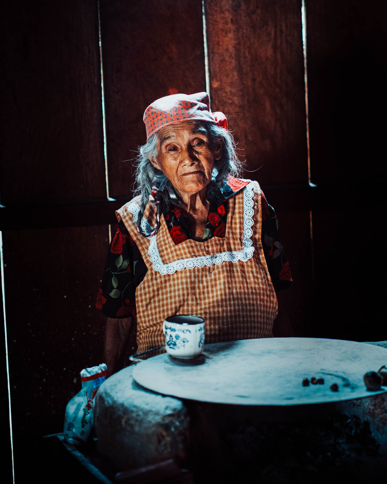 Elderly woman in a headscarf with a cup of coffee in her kitchen in Mexico