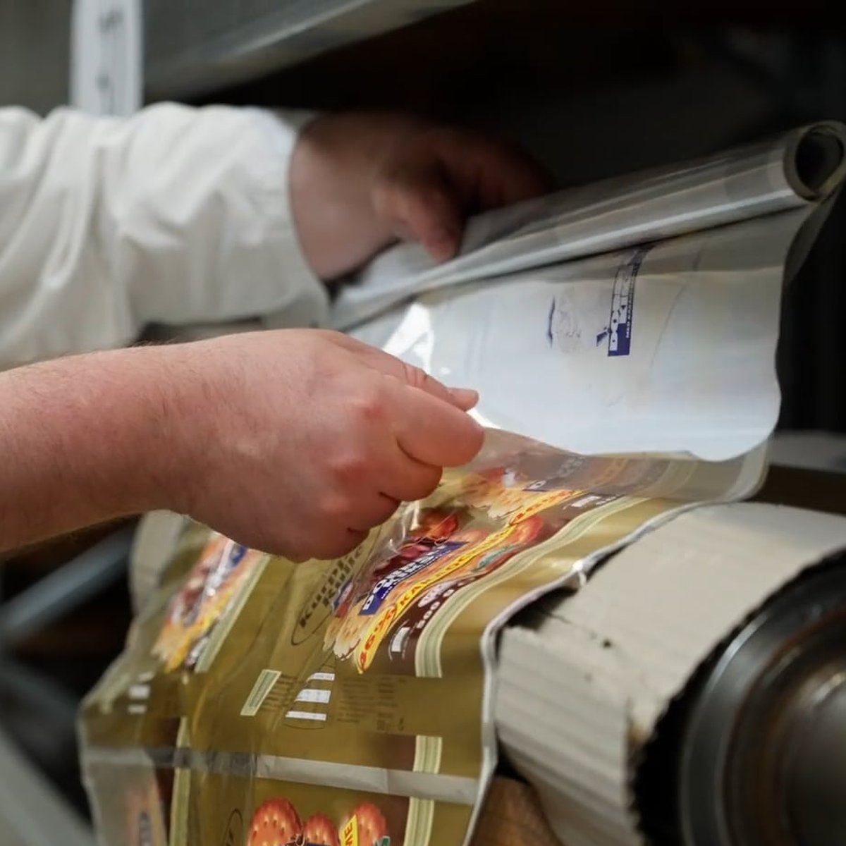 Hands guiding printed packaging film onto a roll at VitraPack