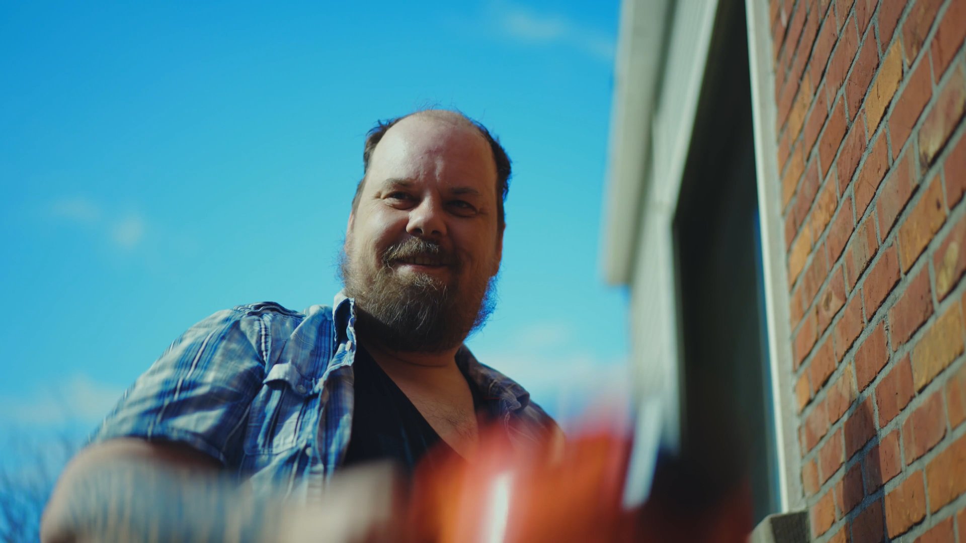 Construction worker smiling down at the camera next to a brick wall, from the Vivaldis campaign film