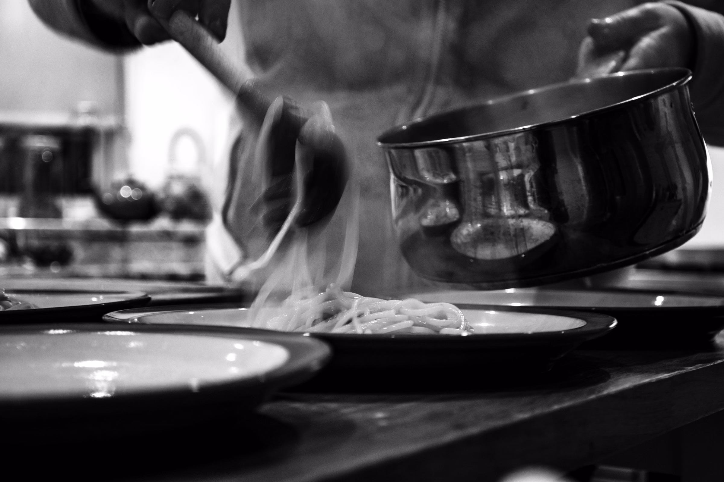 Pasta being lifted from a pan onto a plate with motion blur, in black and white